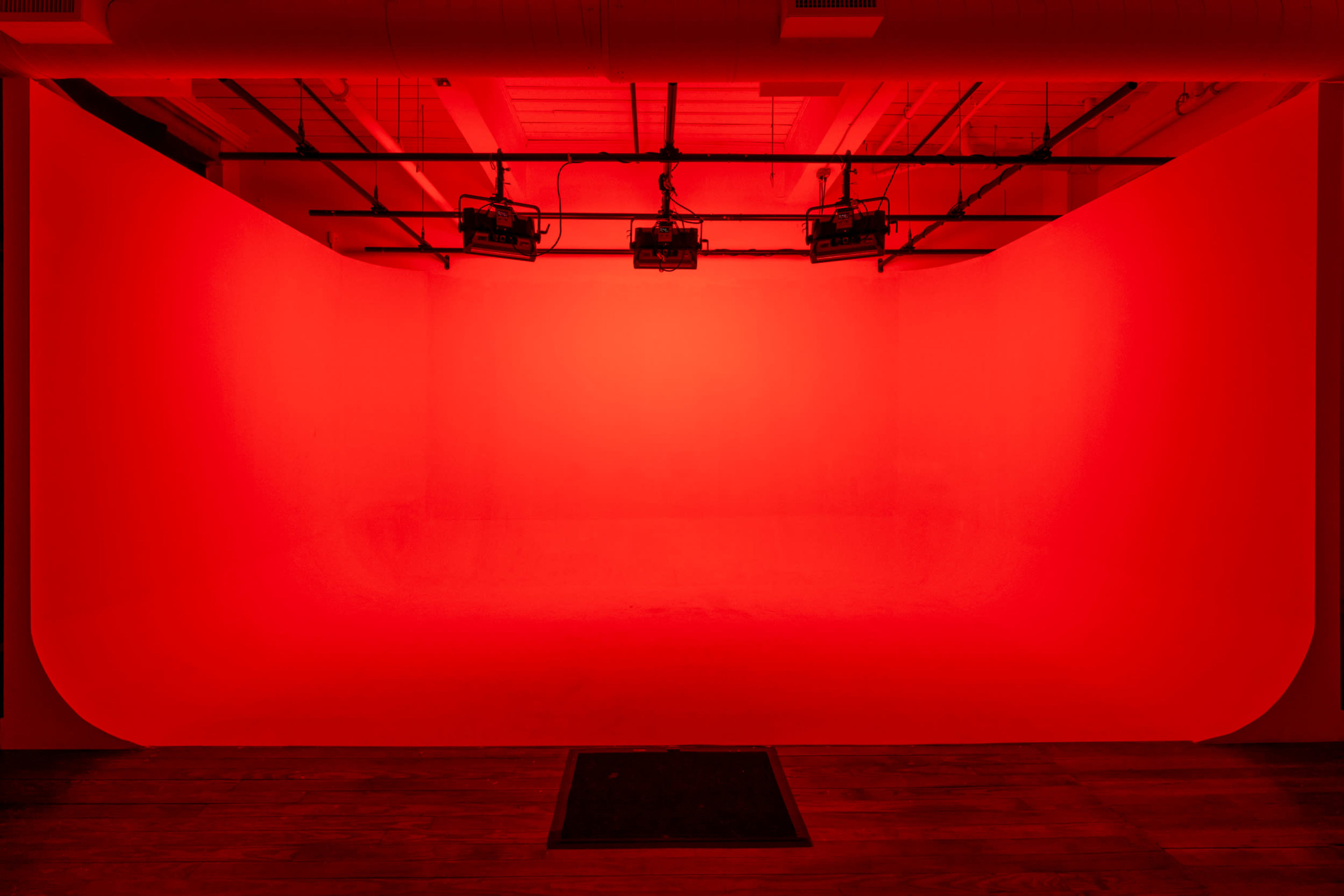 A studio space with a seamless red backdrop and overhead lighting fixtures.