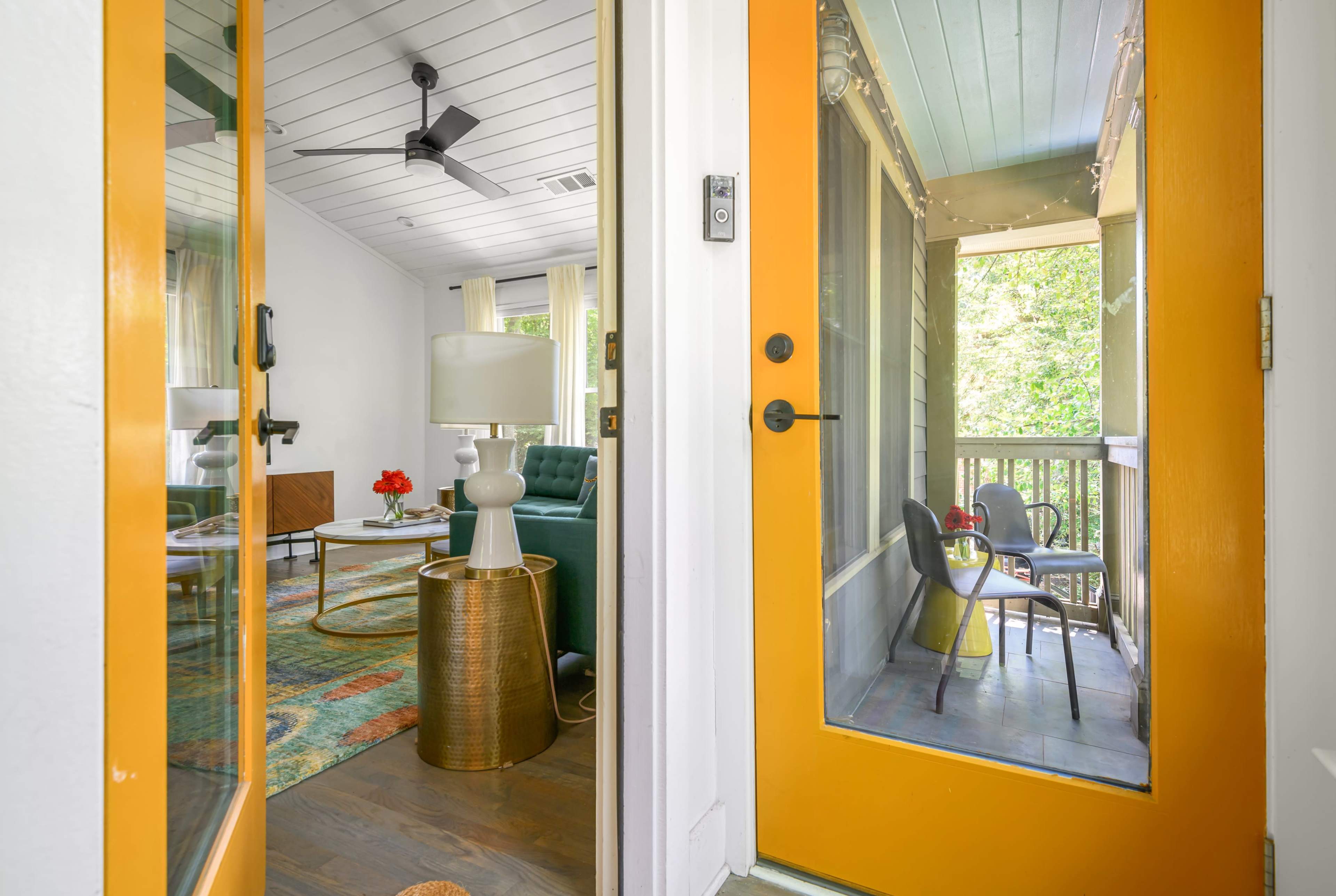 The image shows an entryway with yellow doors leading into a stylish living room and a balcony visible through the glass.