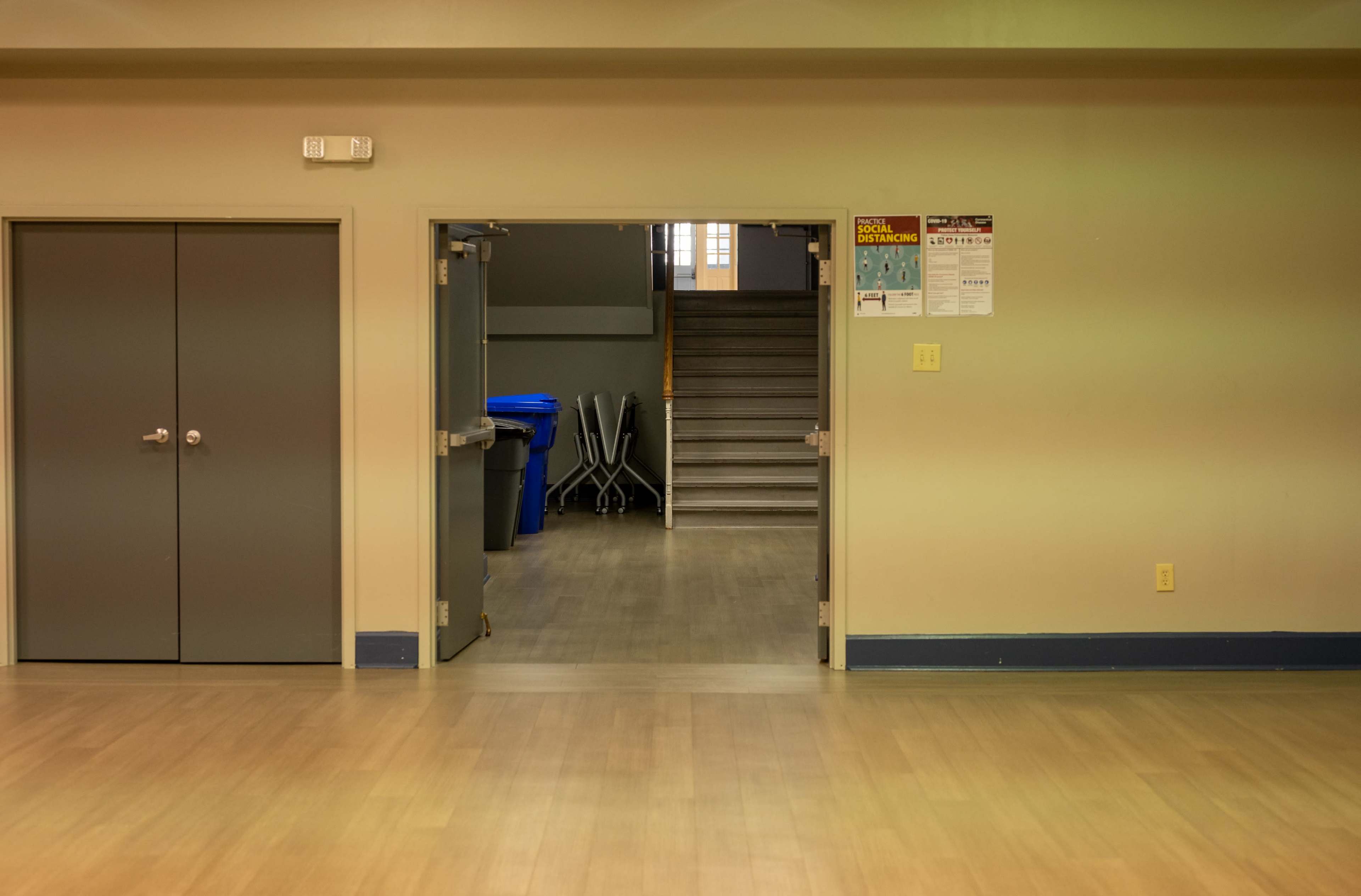 A hallway with a doorway leading to a staircase, flanked by closed double doors and trash bins.