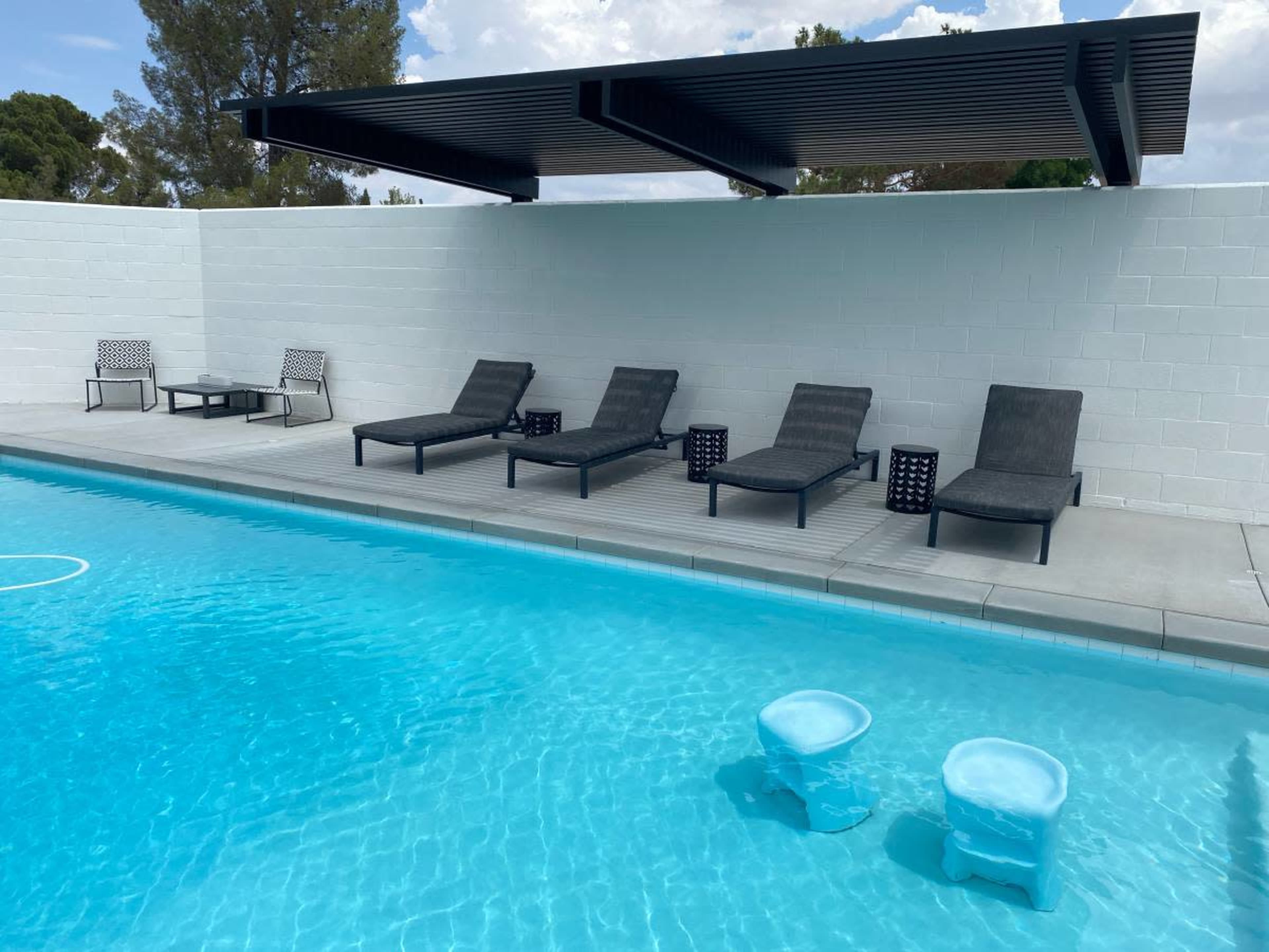 A modern swimming pool with five lounge chairs and two small tables on the deck beside the water.