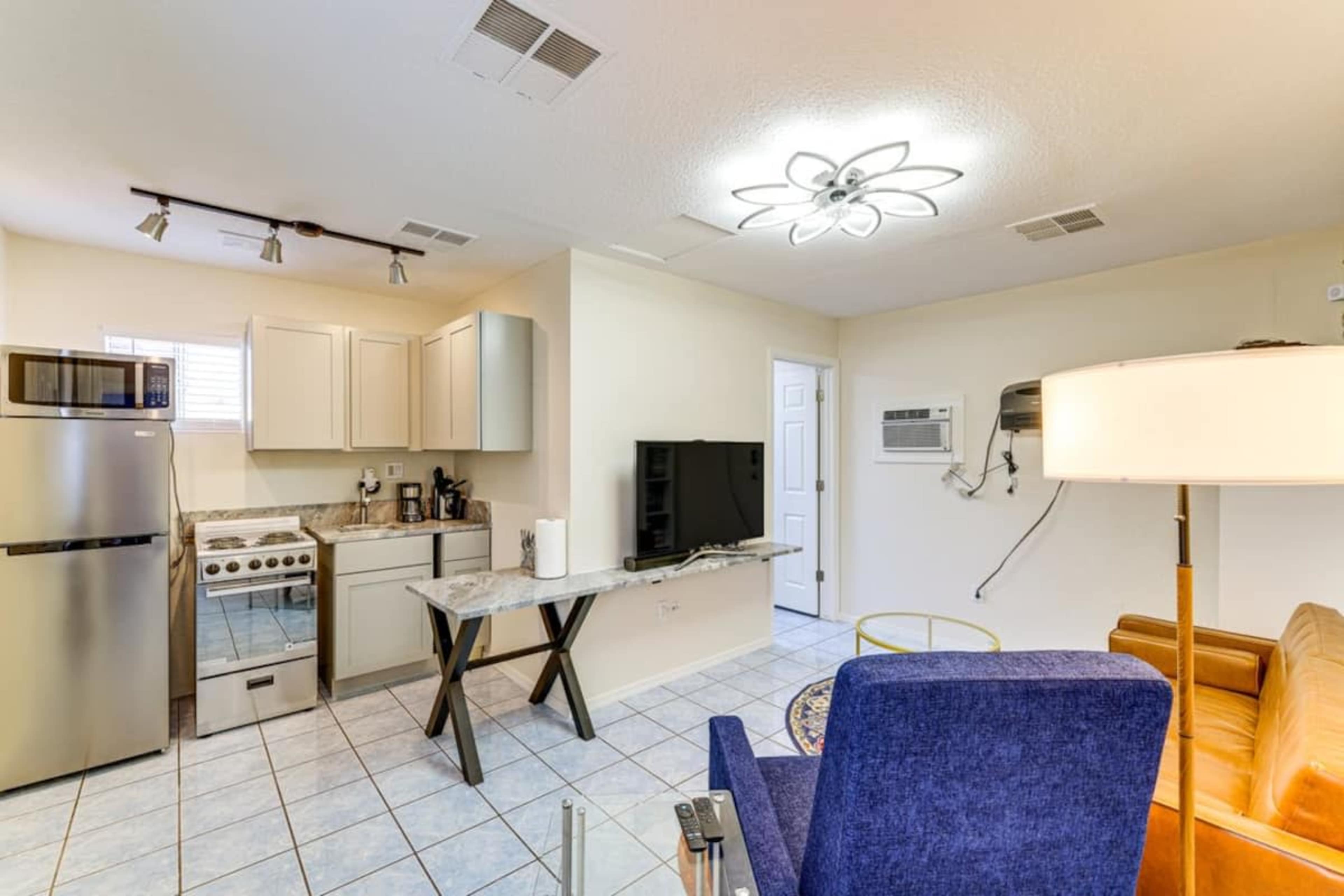 The image shows a compact kitchen and living area with stainless steel appliances, a television, and a sofa, all arranged in a well-lit space.