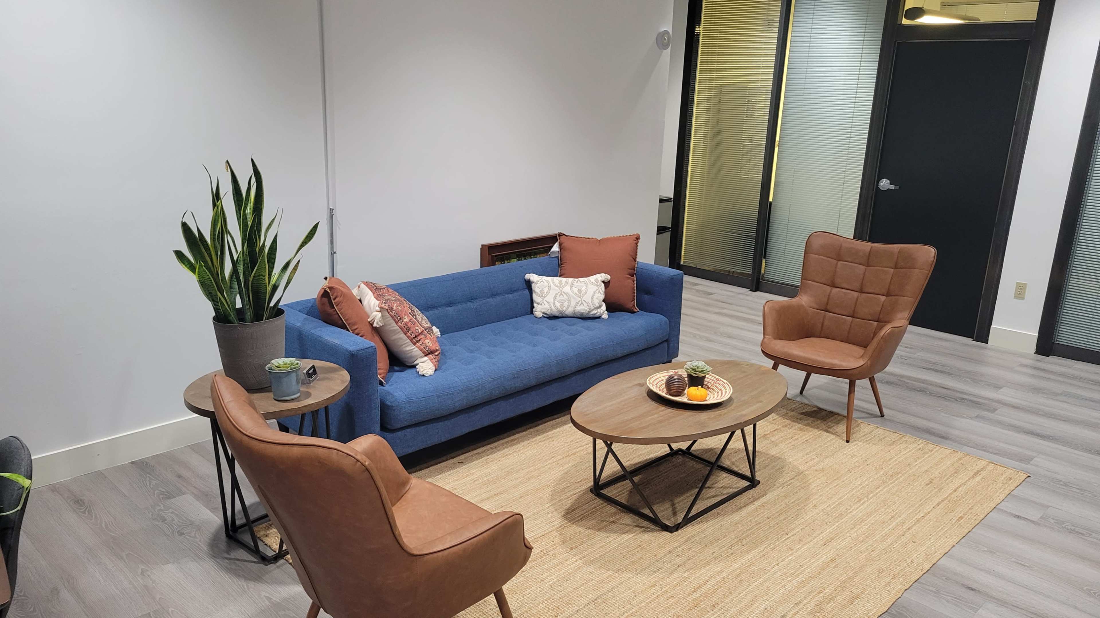 A modern room with a blue sofa, two brown armchairs, and a round coffee table, all arranged on a light-colored rug.
