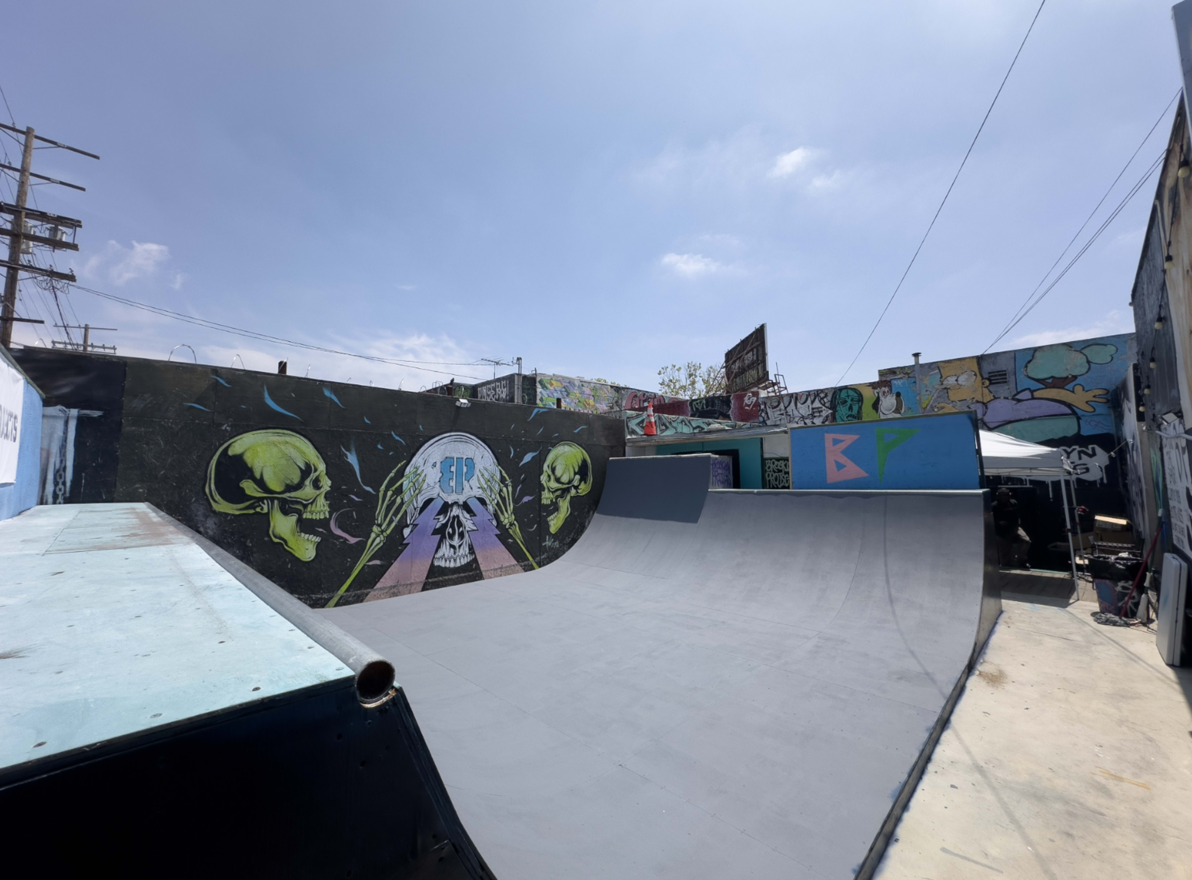 The image shows a skate park ramp with colorful graffiti on the surrounding walls under a clear blue sky.