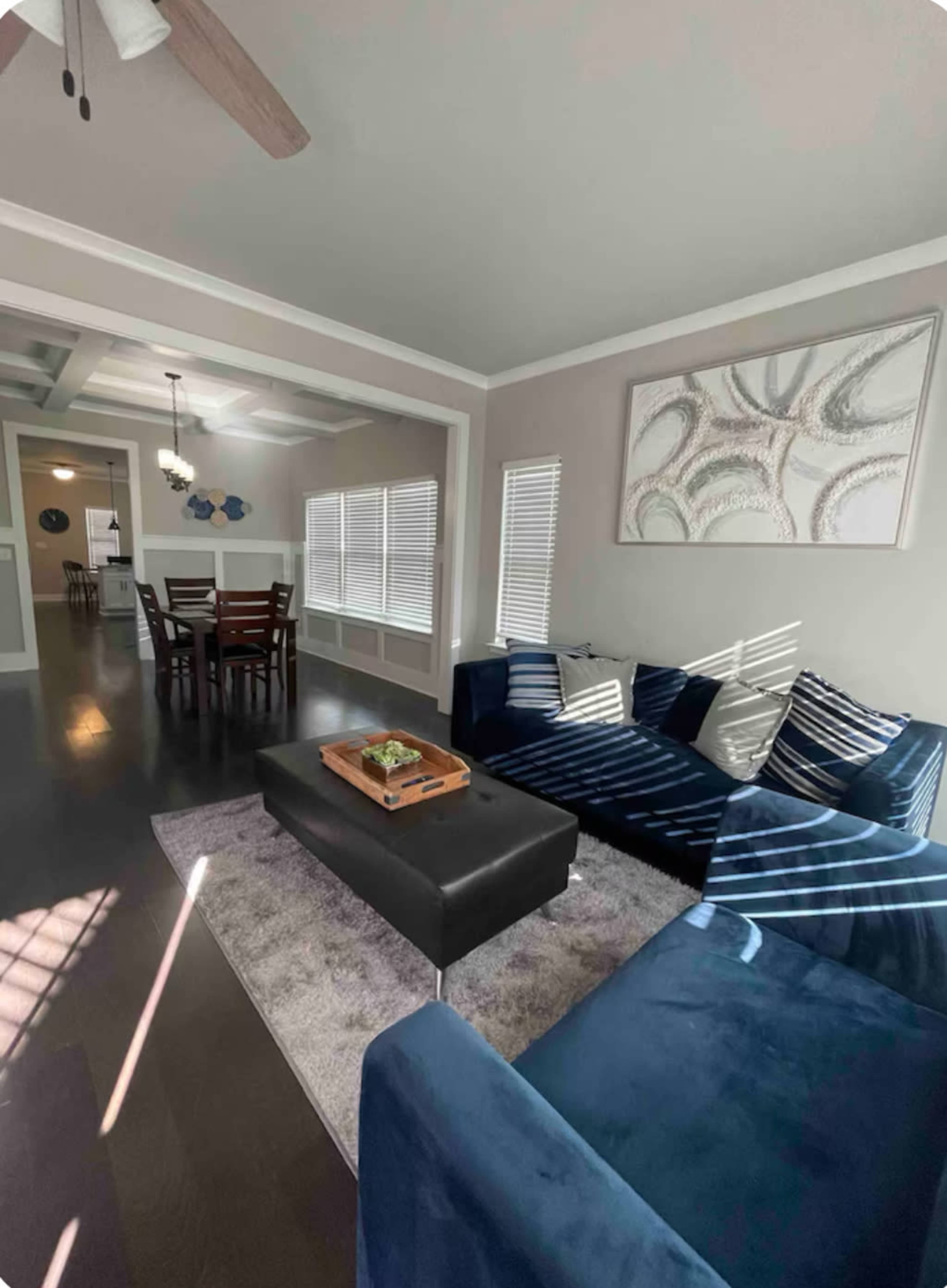 The image shows a modern living room with a blue sectional couch, a coffee table in the center, and a dining area visible in the background.