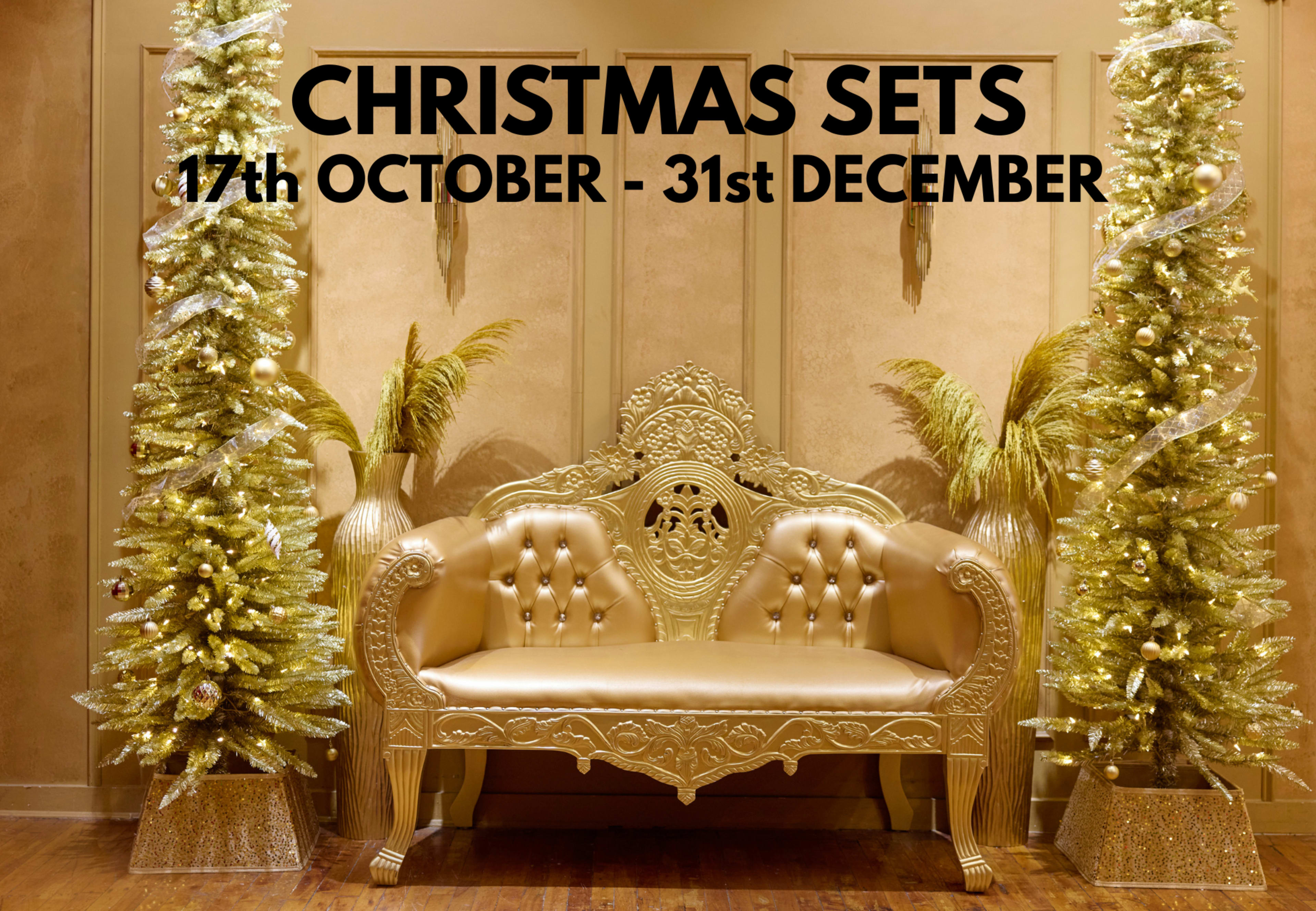 The image features a luxurious gold-colored couch flanked by two decorated Christmas trees, with a prominent sign announcing "CHRISTMAS SETS" and the dates from October 17th to December 31st.