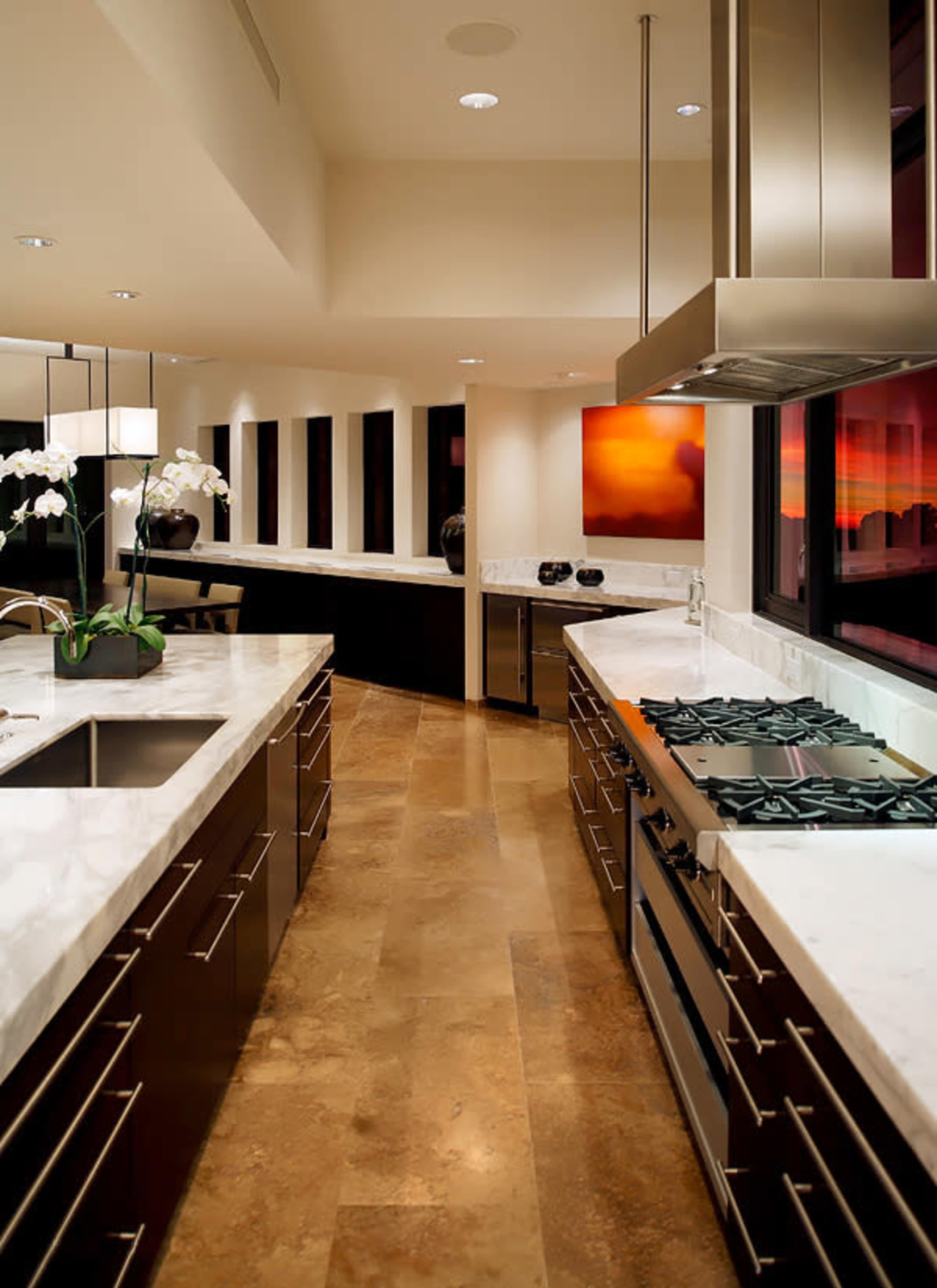A modern kitchen features sleek cabinets, a marble countertop, and a central island with a gas stove, illuminated by overhead lights.