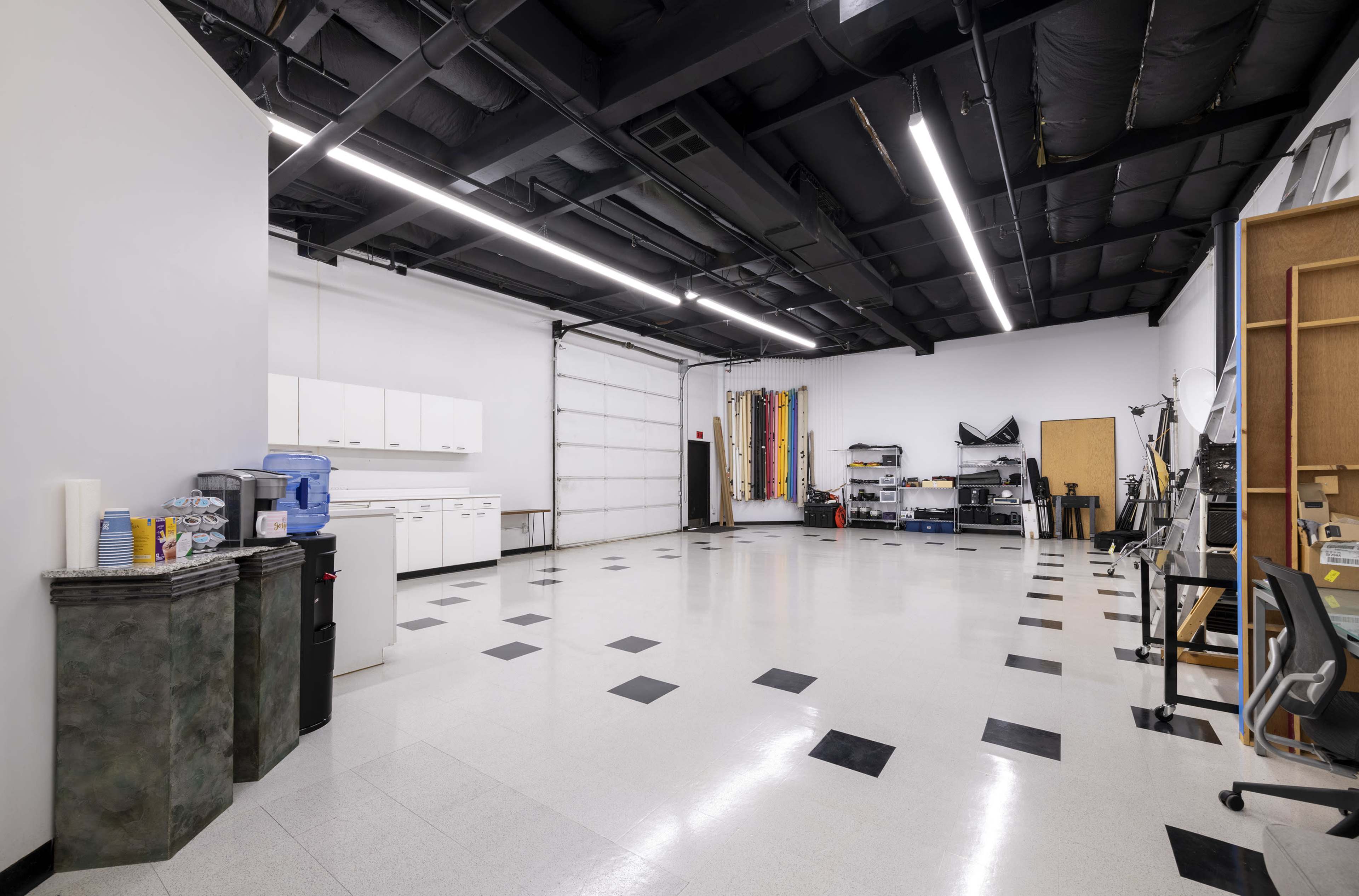 A spacious, well-lit room with a polished floor, featuring cabinets, a water cooler, and various workstations along the walls.