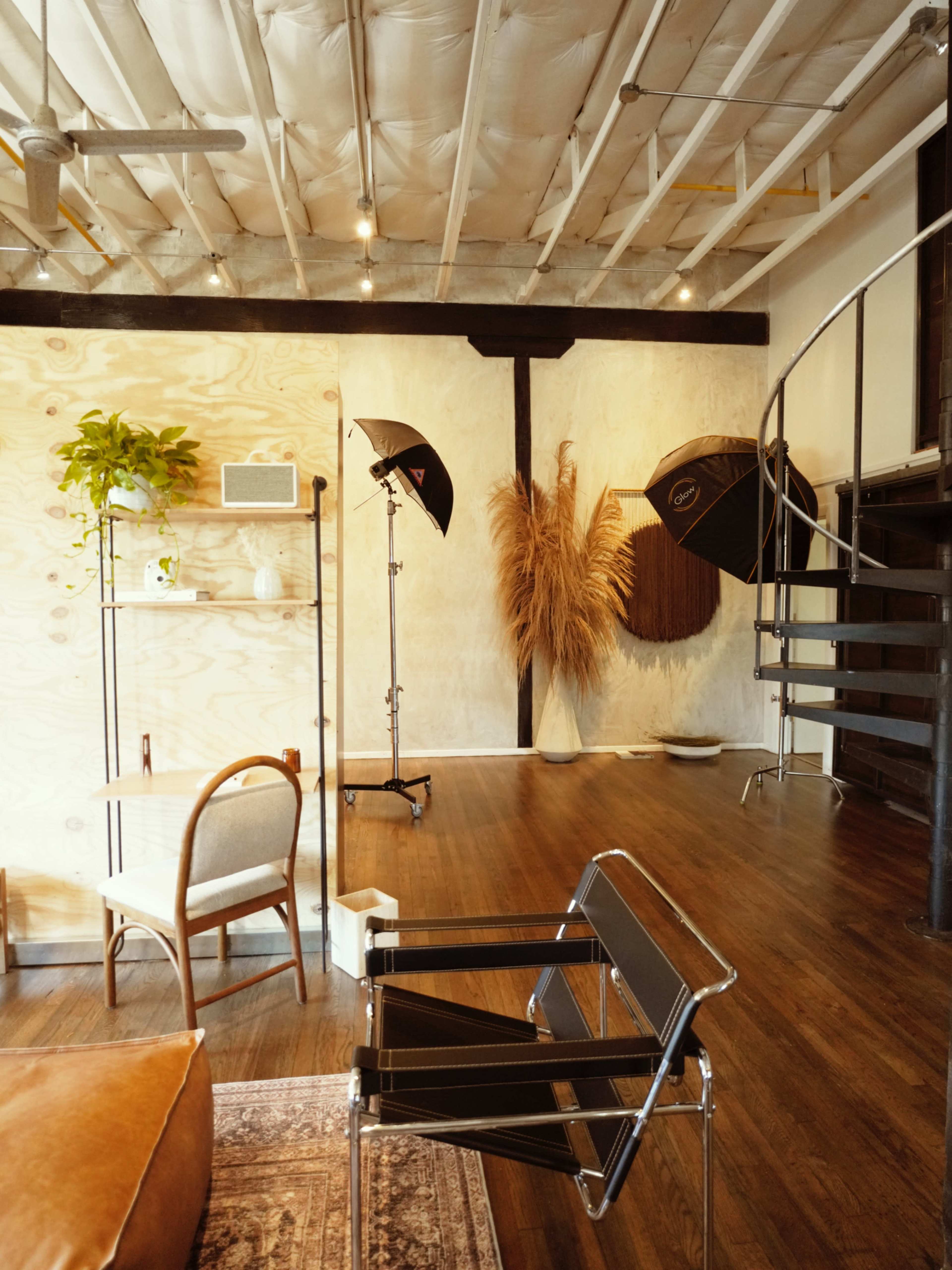 The image shows a spacious interior featuring a mix of modern and natural elements, including a spiral staircase, photography equipment, and decorative plants.