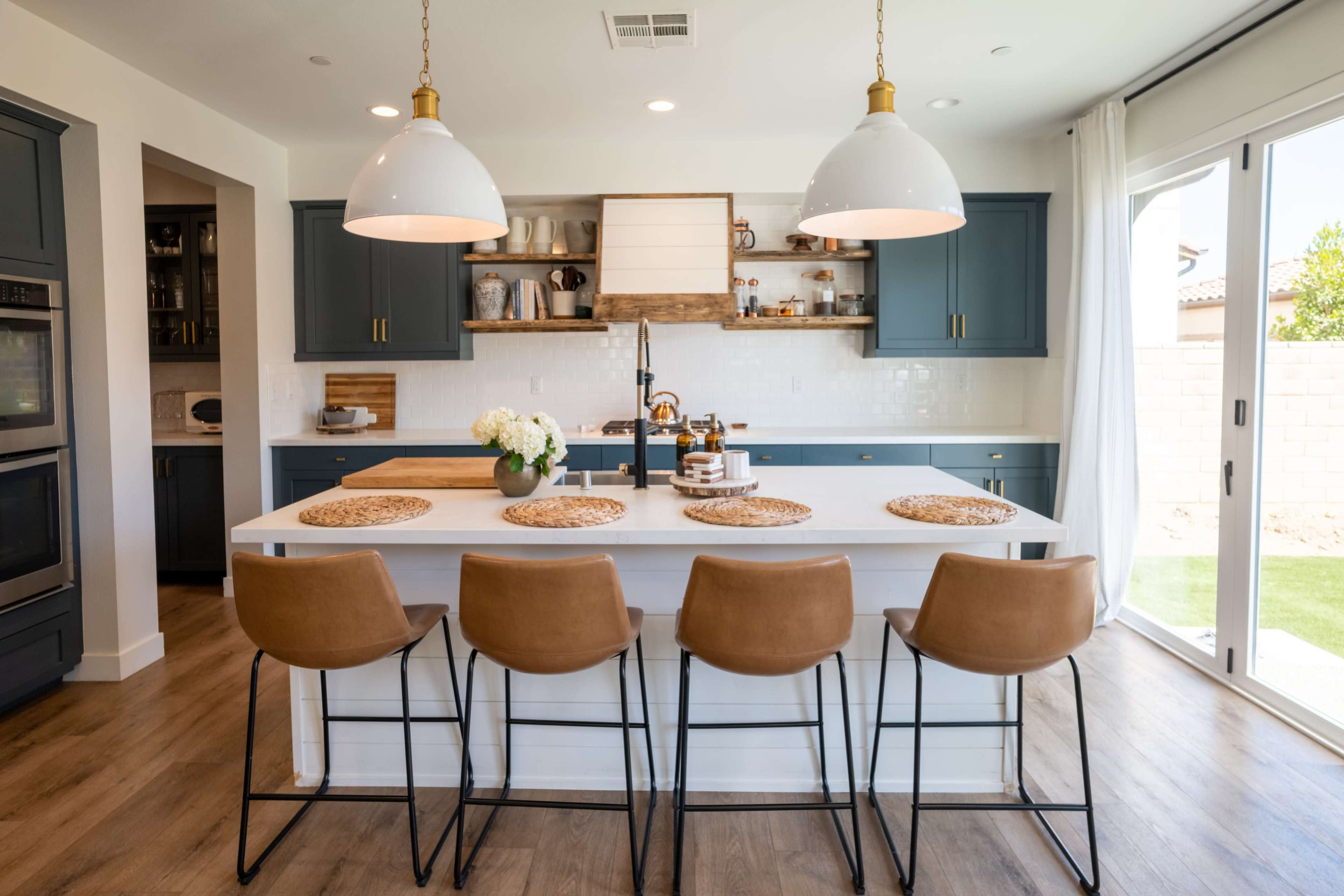 A modern kitchen featuring blue cabinets, a large white island with four brown bar stools, and pendant lighting above.