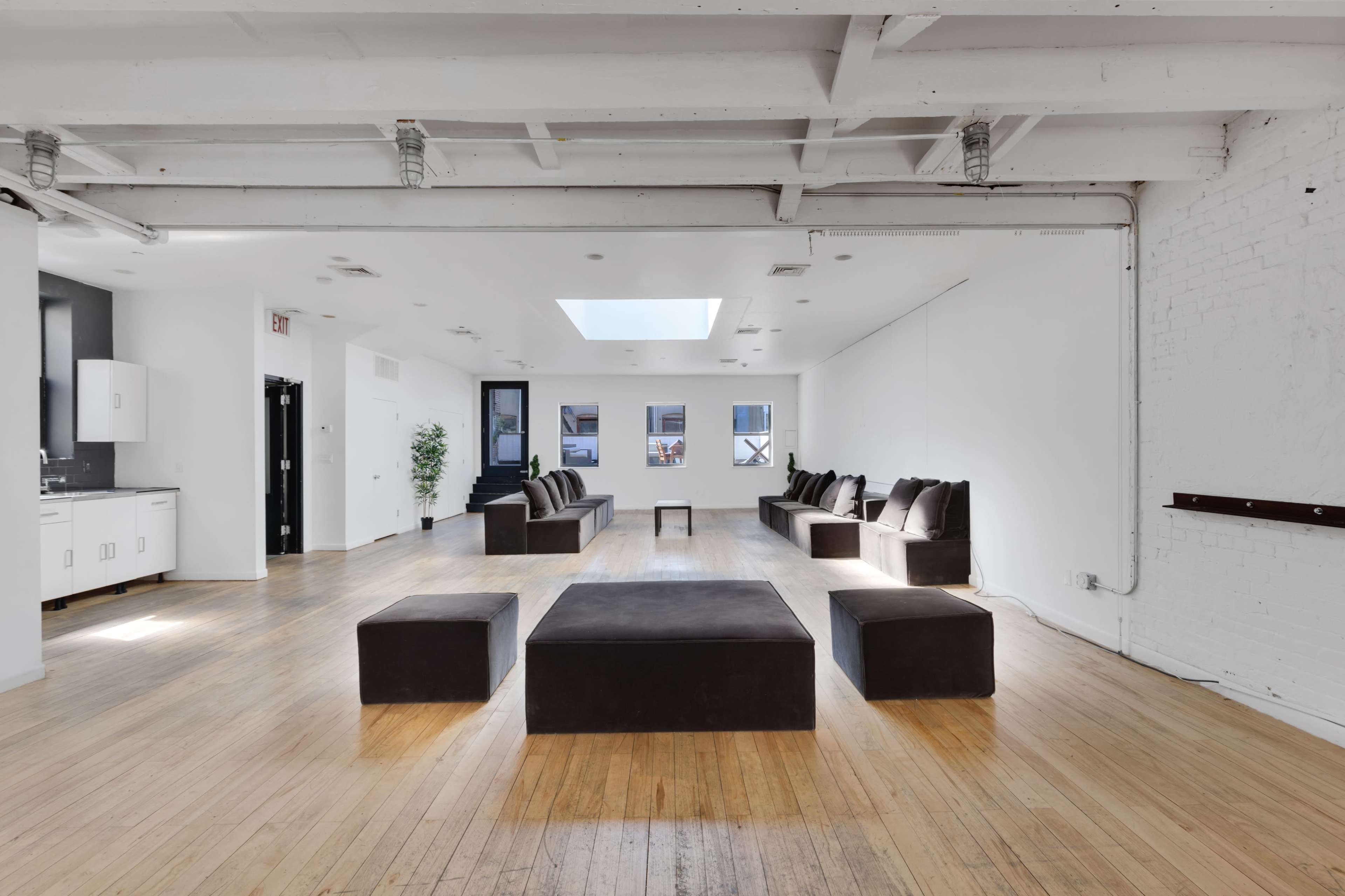 A spacious, minimalist room with wooden floors, a skylight, and several low seating areas arranged around a central table.
