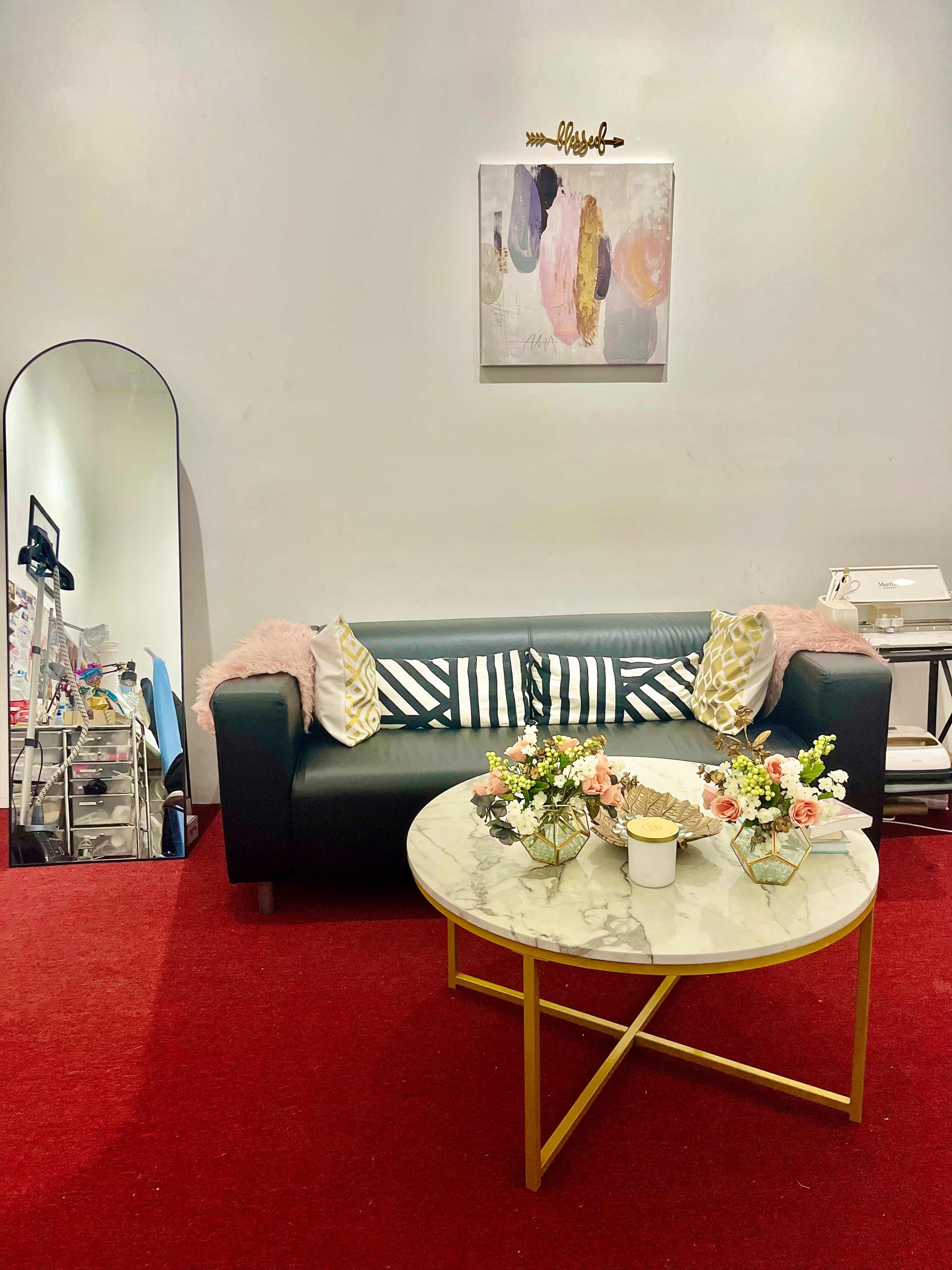 A cozy seating area with a dark leather couch, striped pillows, a marble-topped coffee table decorated with flowers, and a large mirror against a light-colored wall.