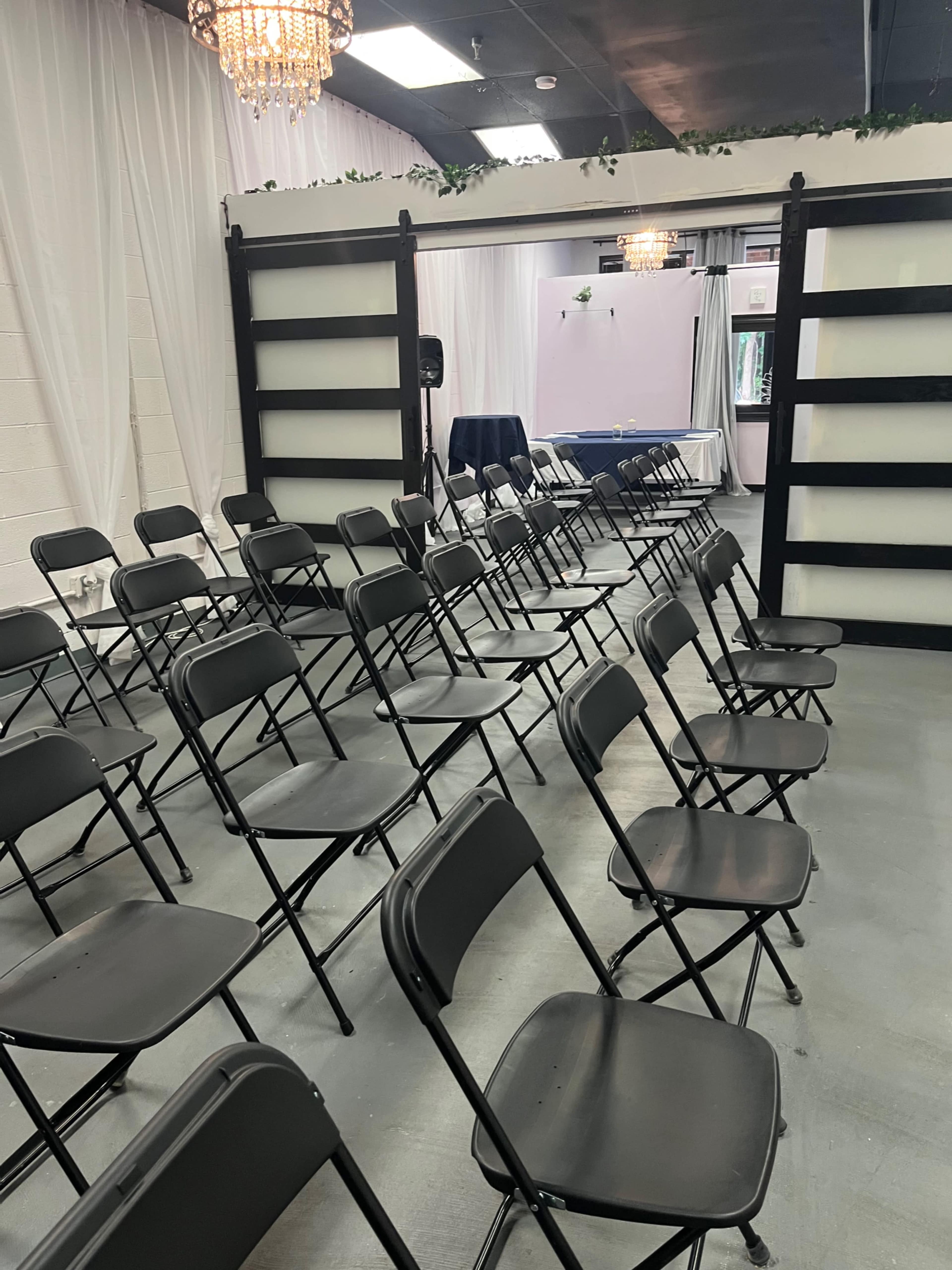 The image shows a set of black folding chairs arranged in rows facing a decorative back wall inside an indoor event space.