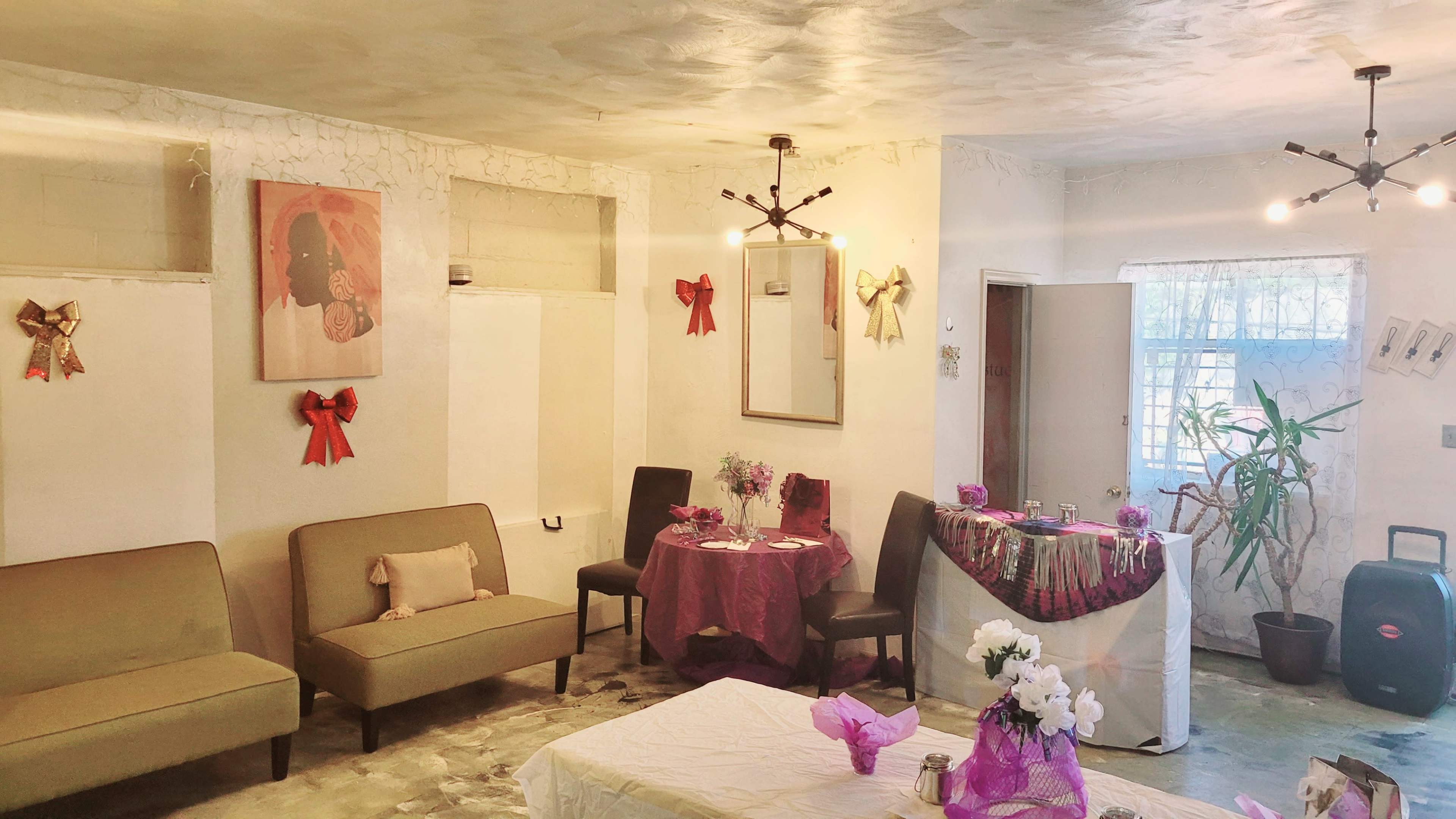 A decorated indoor space featuring two brown sofas, a table with a white tablecloth, and floral arrangements, along with festive bows on the walls.