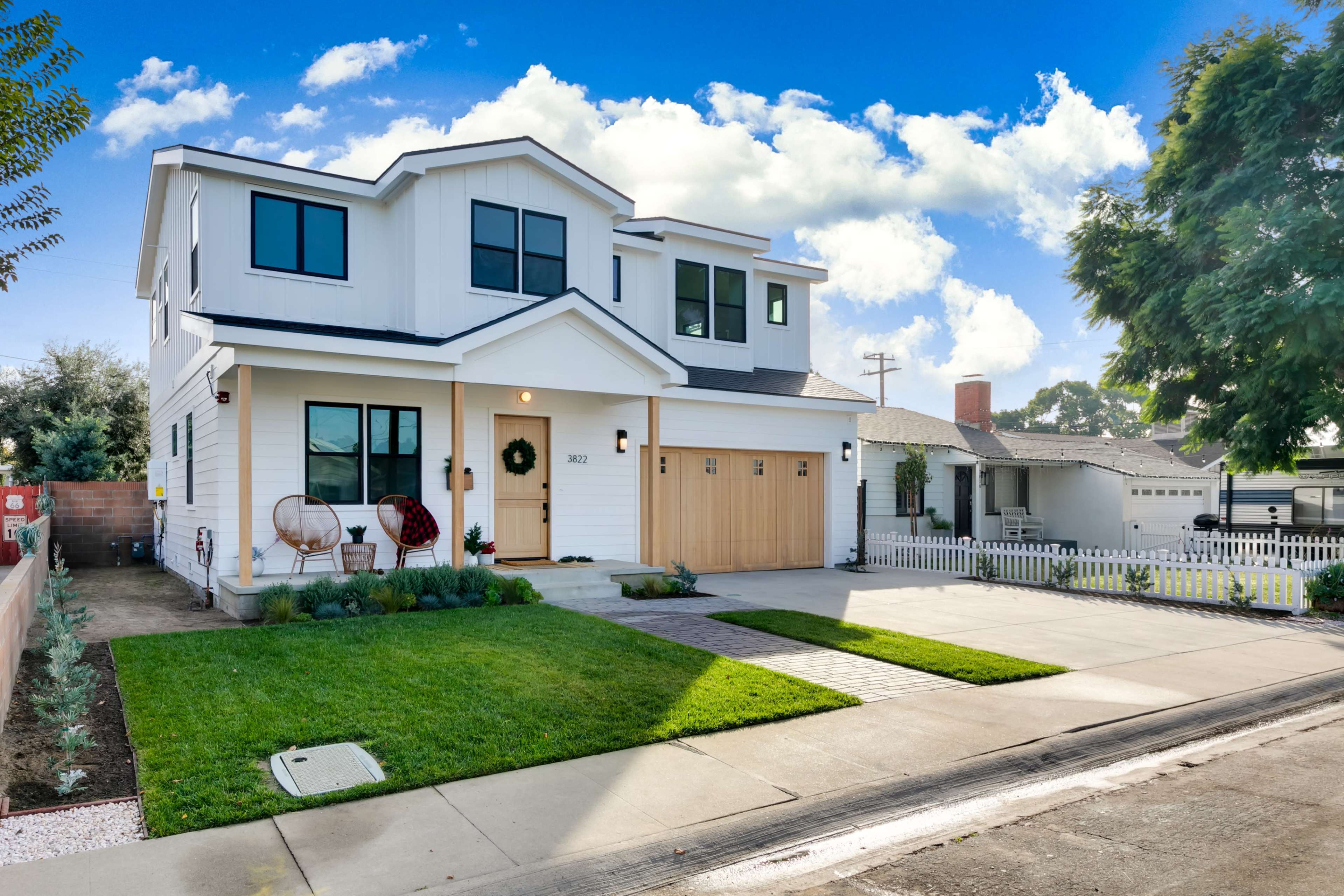 A two-story, modern residential home with a white exterior, a wooden garage door, and a neatly maintained front yard.