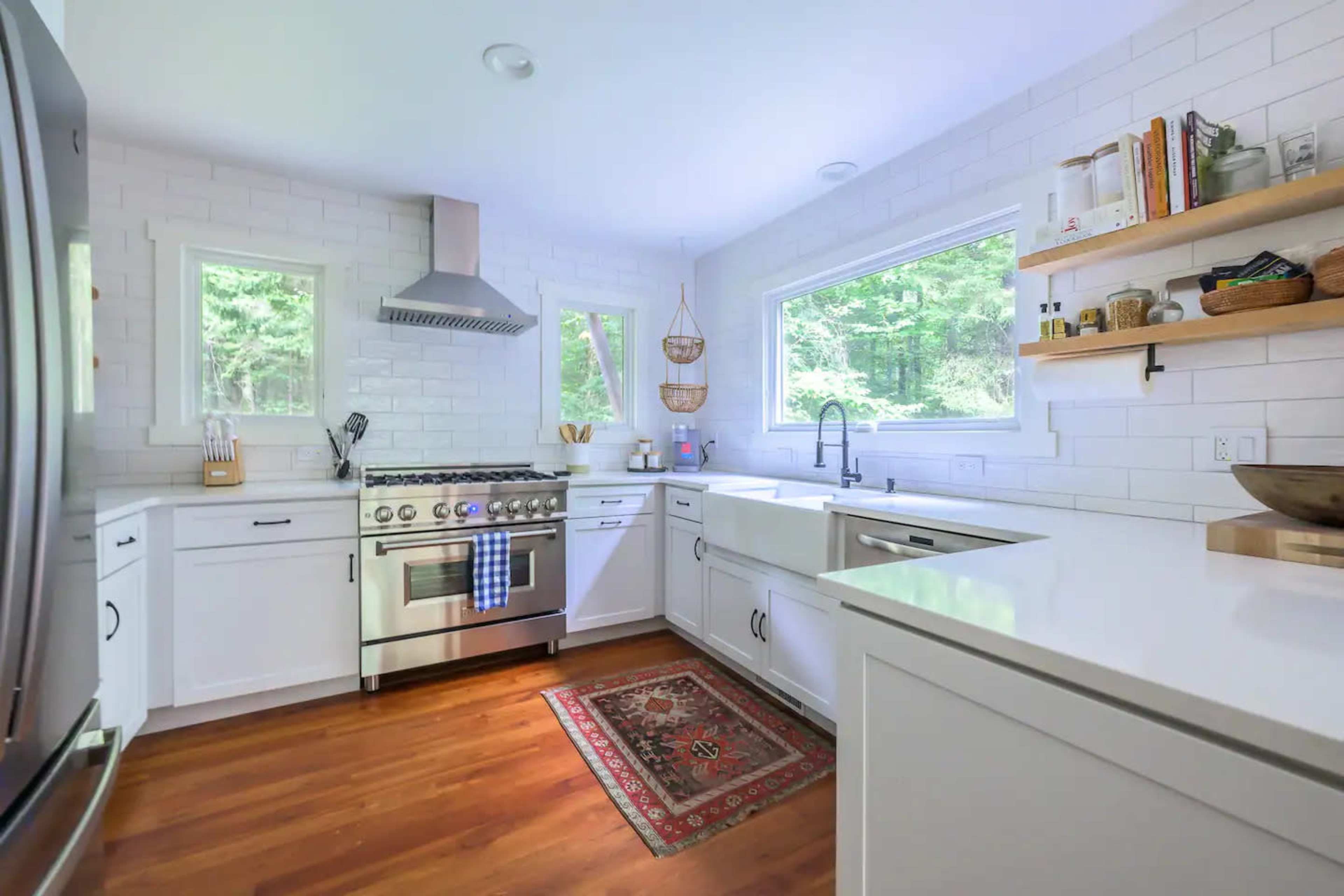 A modern kitchen features stainless steel appliances, white cabinetry, and a wooden floor with a patterned rug.