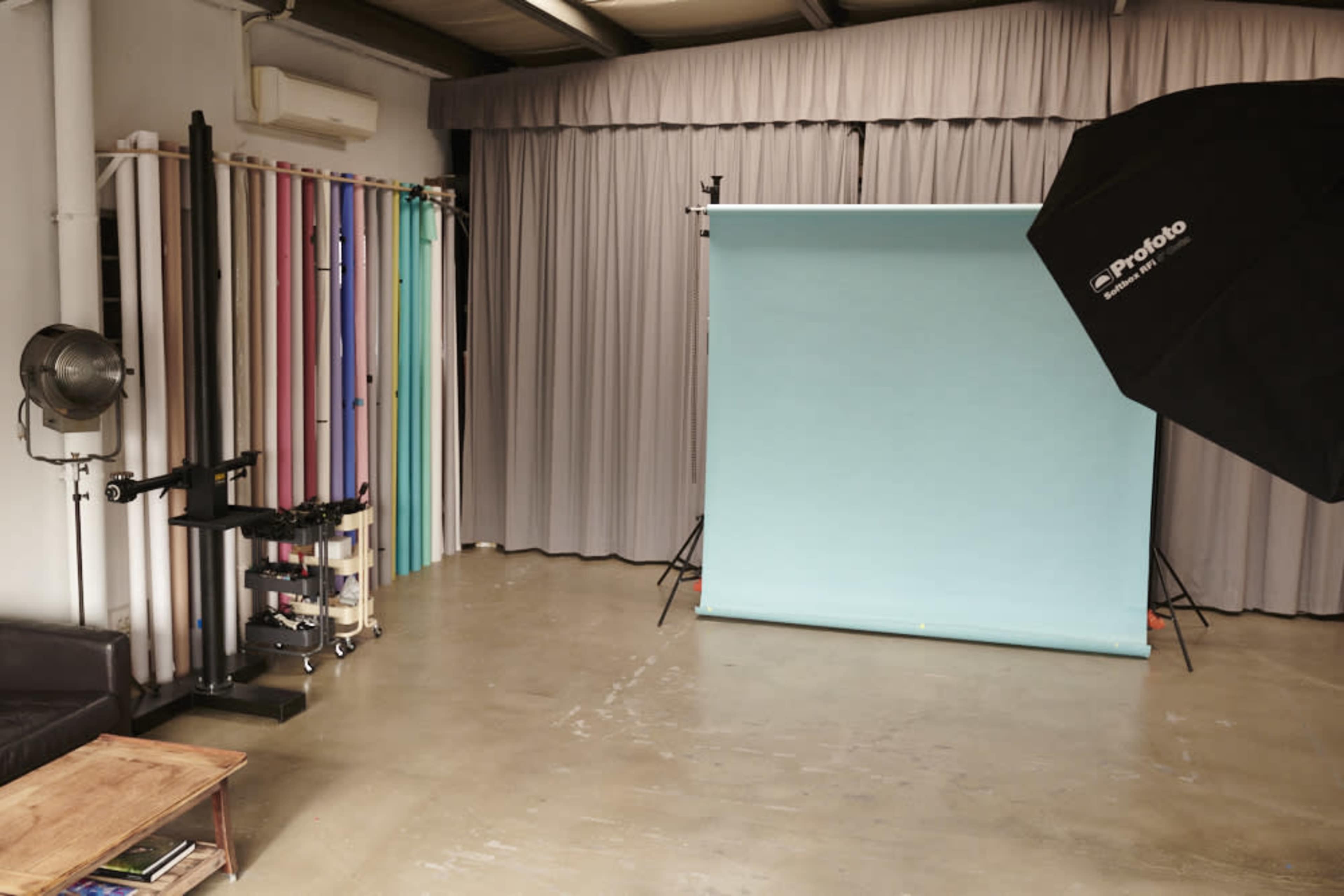 A photography studio with a blue backdrop, colored paper rolls, a fan, and a lighting umbrella.