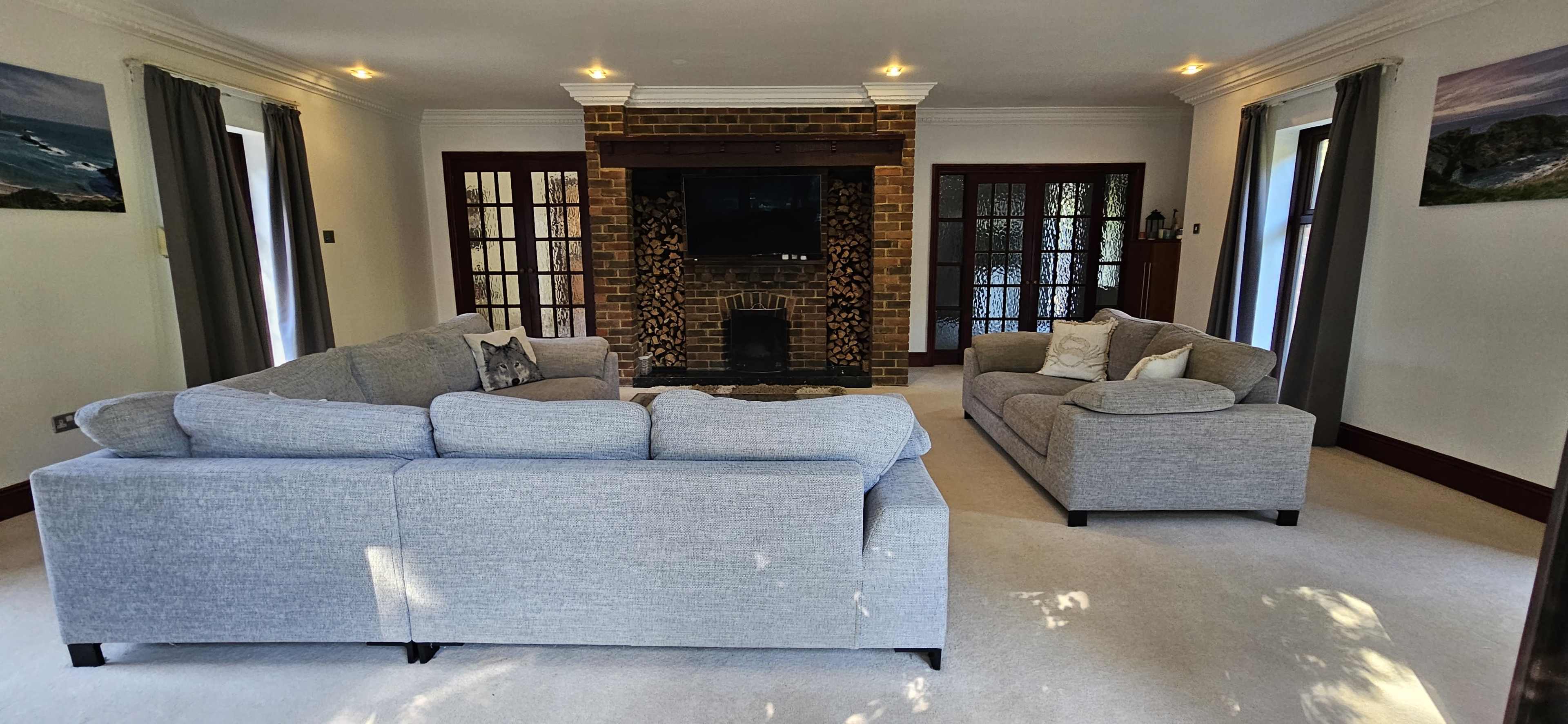 The living room features a gray sectional sofa and a matching couch facing a brick fireplace set against white walls with large windows.