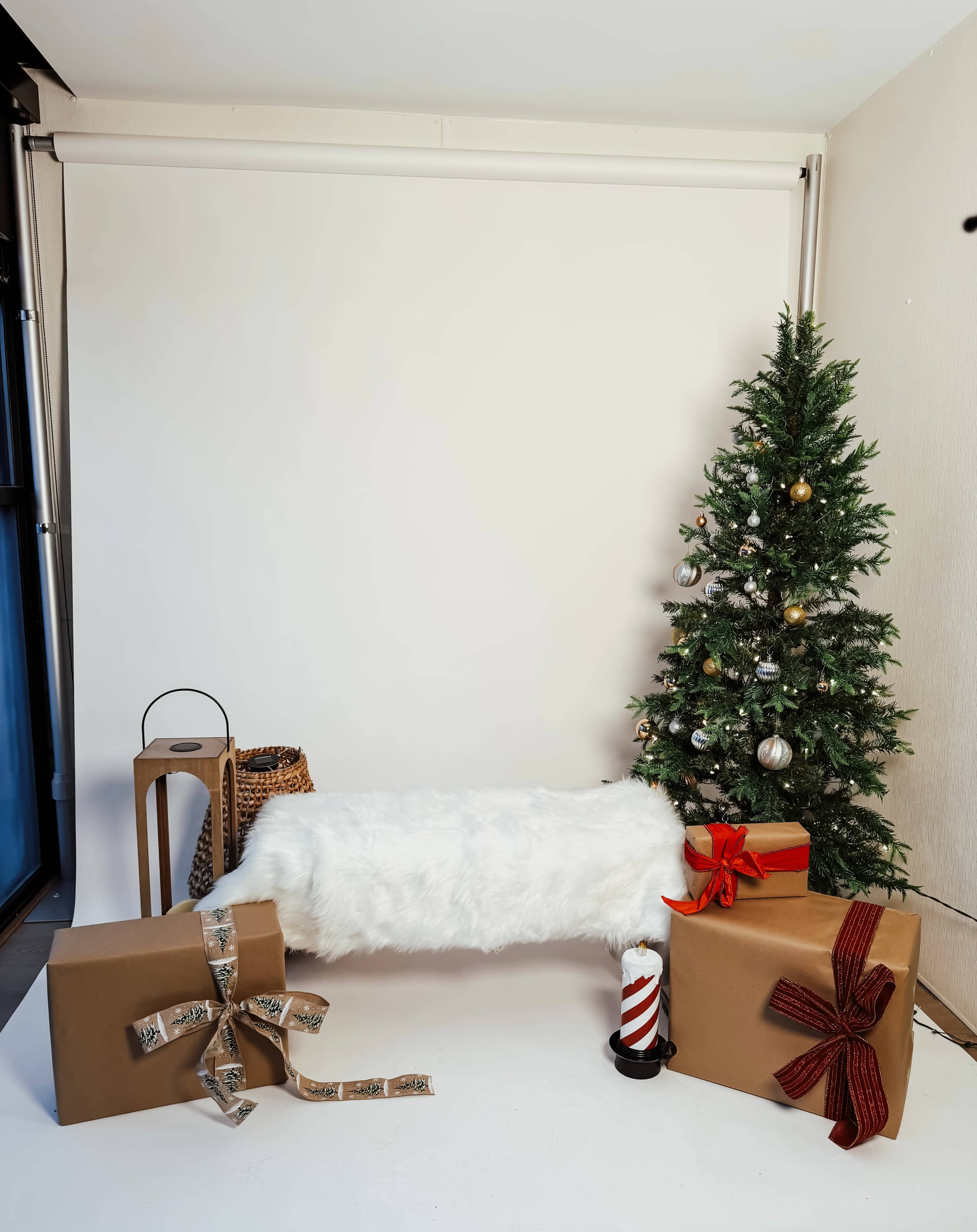 The scene features a white backdrop with a Christmas tree adorned with ornaments, surrounded by wrapped gifts and a fluffy white bench.