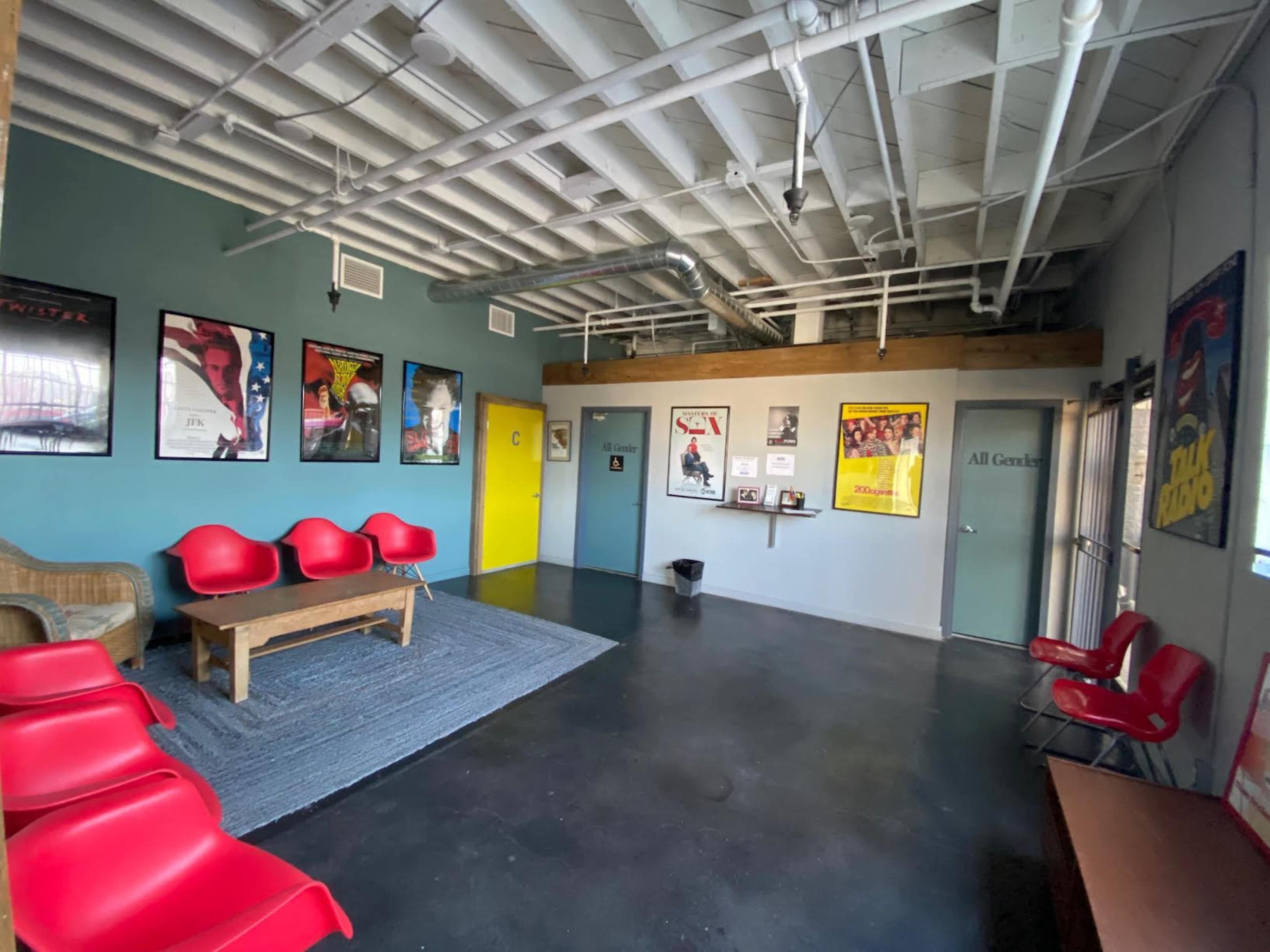 A waiting area with red chairs, a wooden table, and movie posters on the walls.