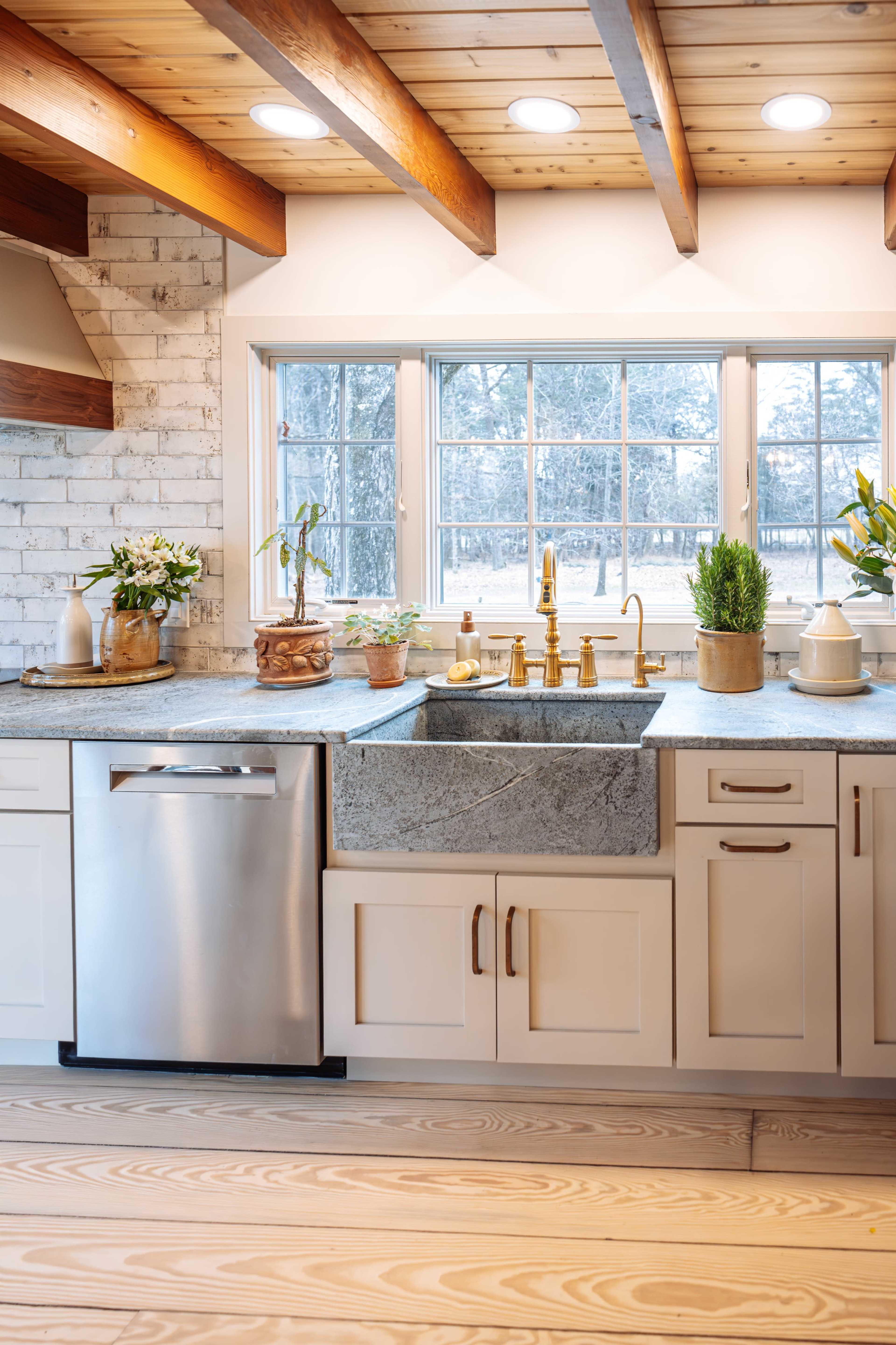 The kitchen features a large window above a farmhouse sink, surrounded by wooden beams and modern appliances.