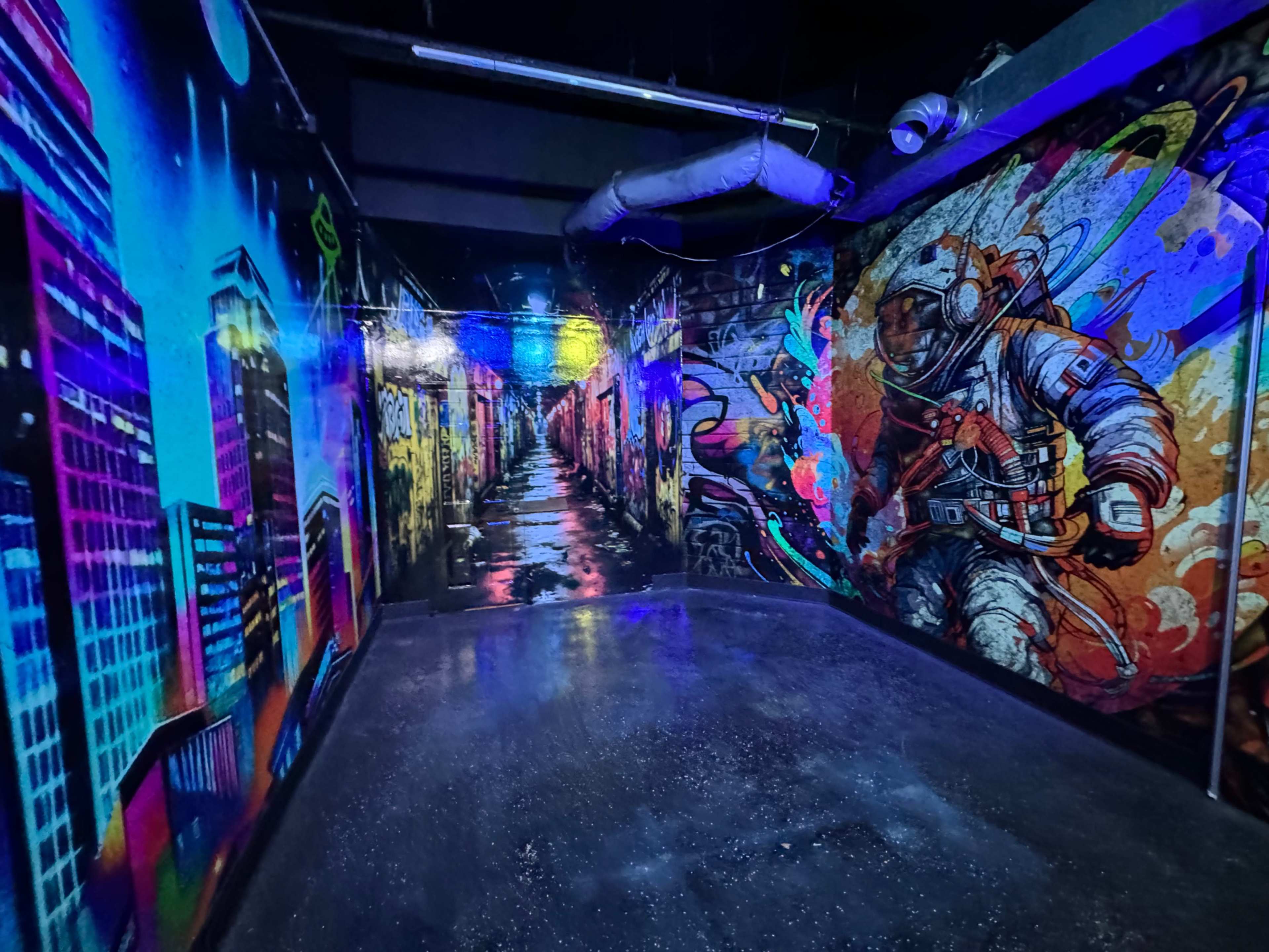 The image shows a dimly lit room with vibrant graffiti murals depicting cityscapes and an astronaut on the walls.