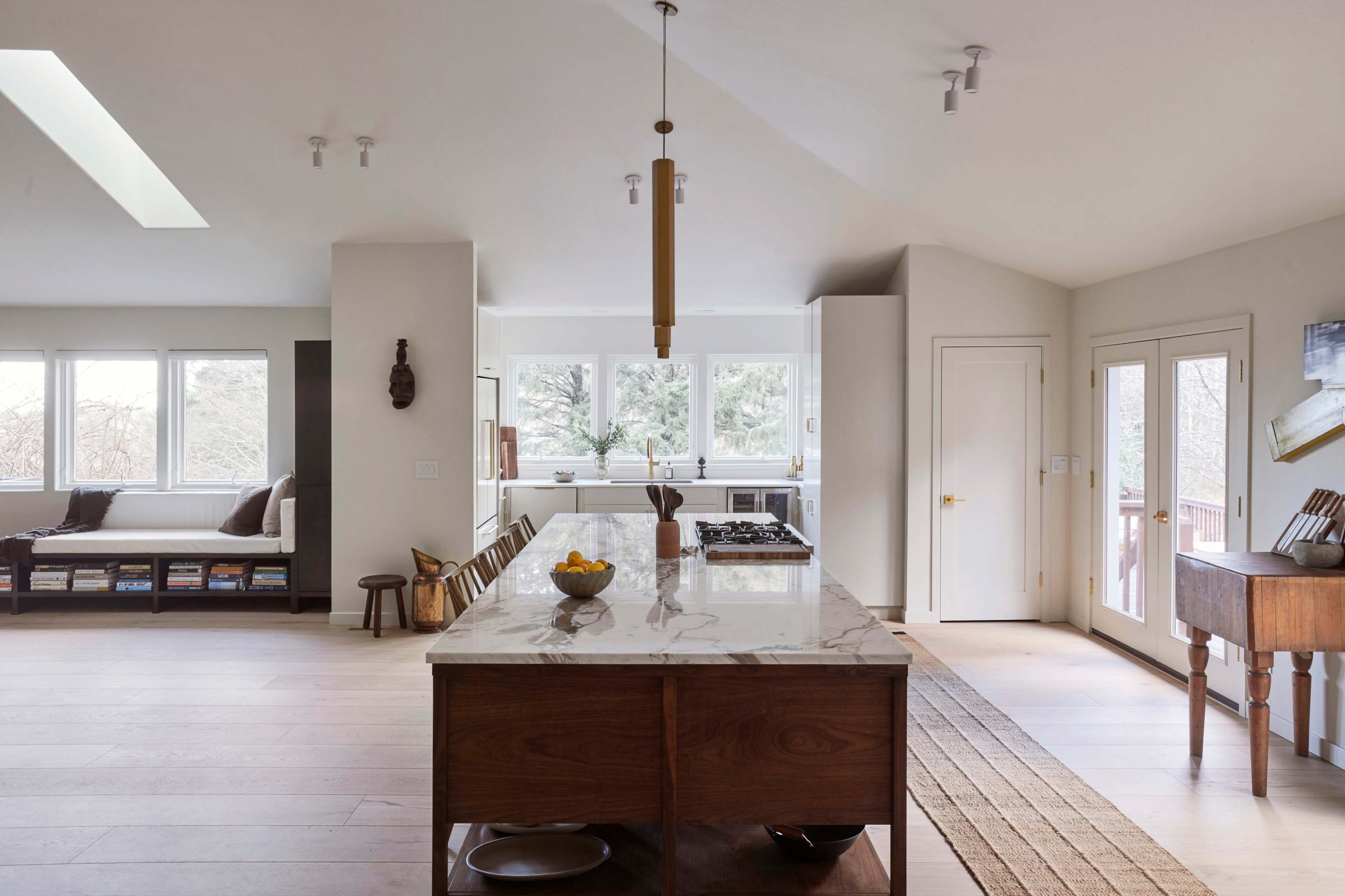 A modern kitchen features a central island with a marble countertop, surrounded by bright windows and minimalistic decor.