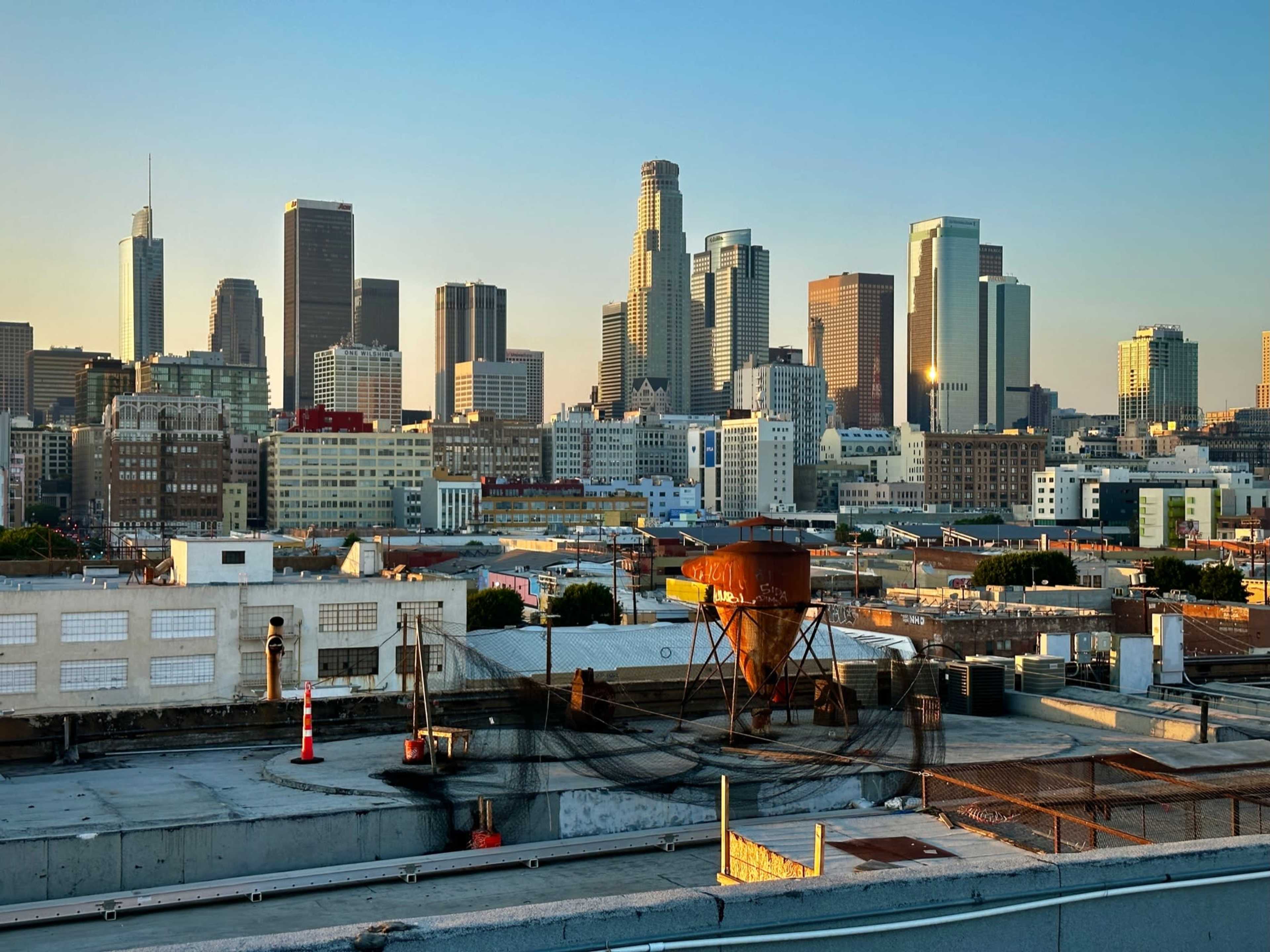 A view of the Los Angeles skyline at sunrise, featuring a mix of modern skyscrapers and industrial buildings.