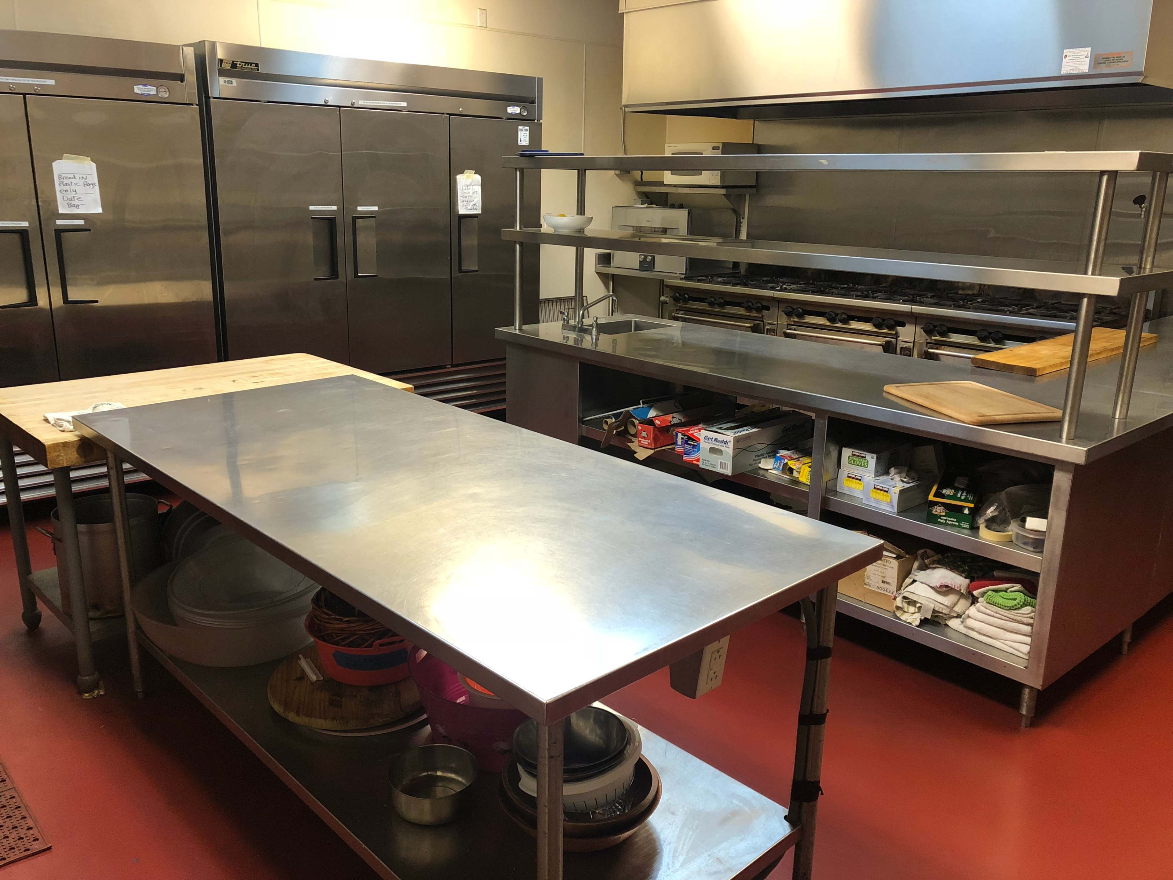 A commercial kitchen with stainless steel appliances, worktables, and storage areas neatly organized.