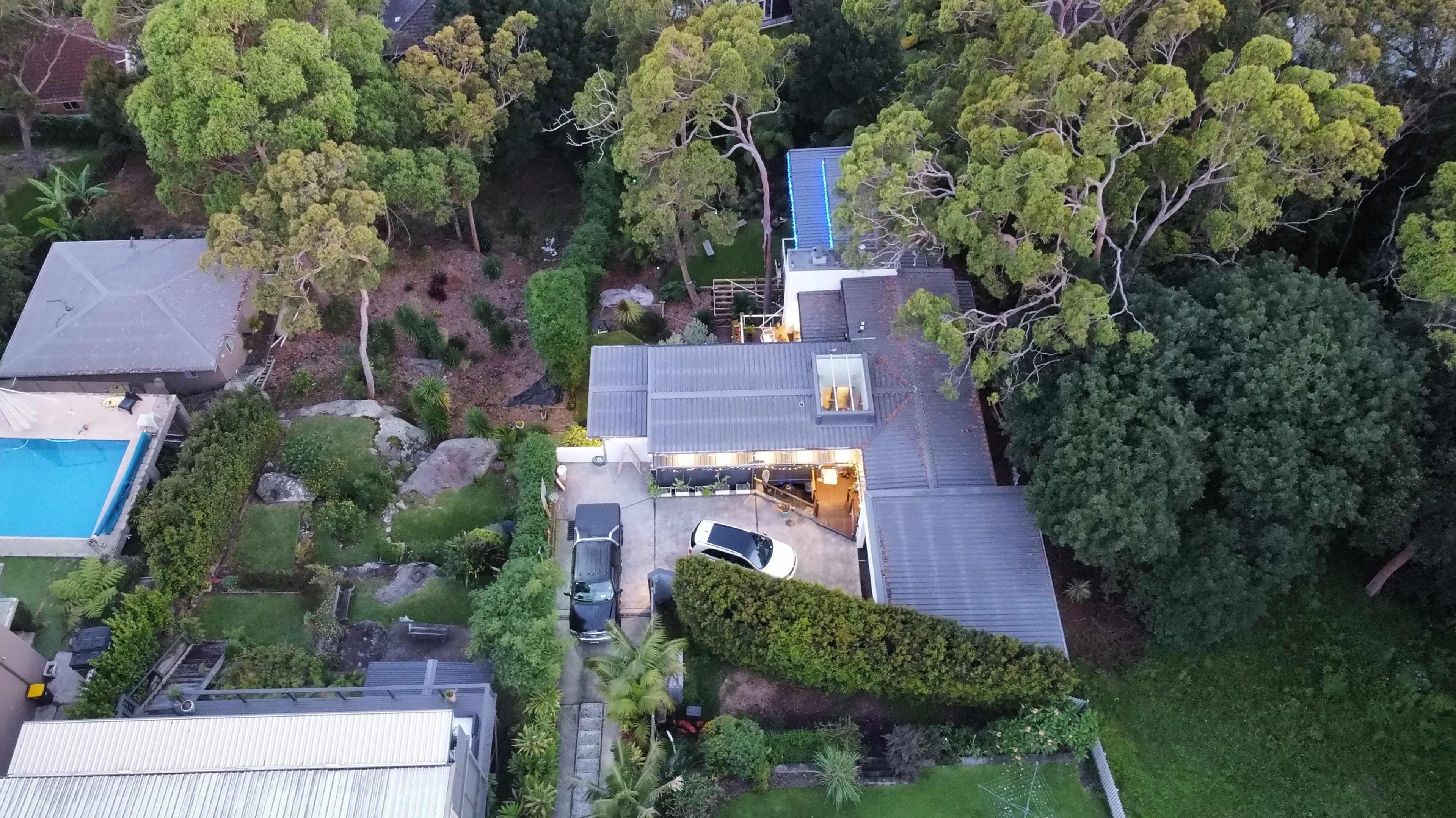 An aerial view shows a residential area with several houses, a swimming pool, and various trees surrounding the properties.