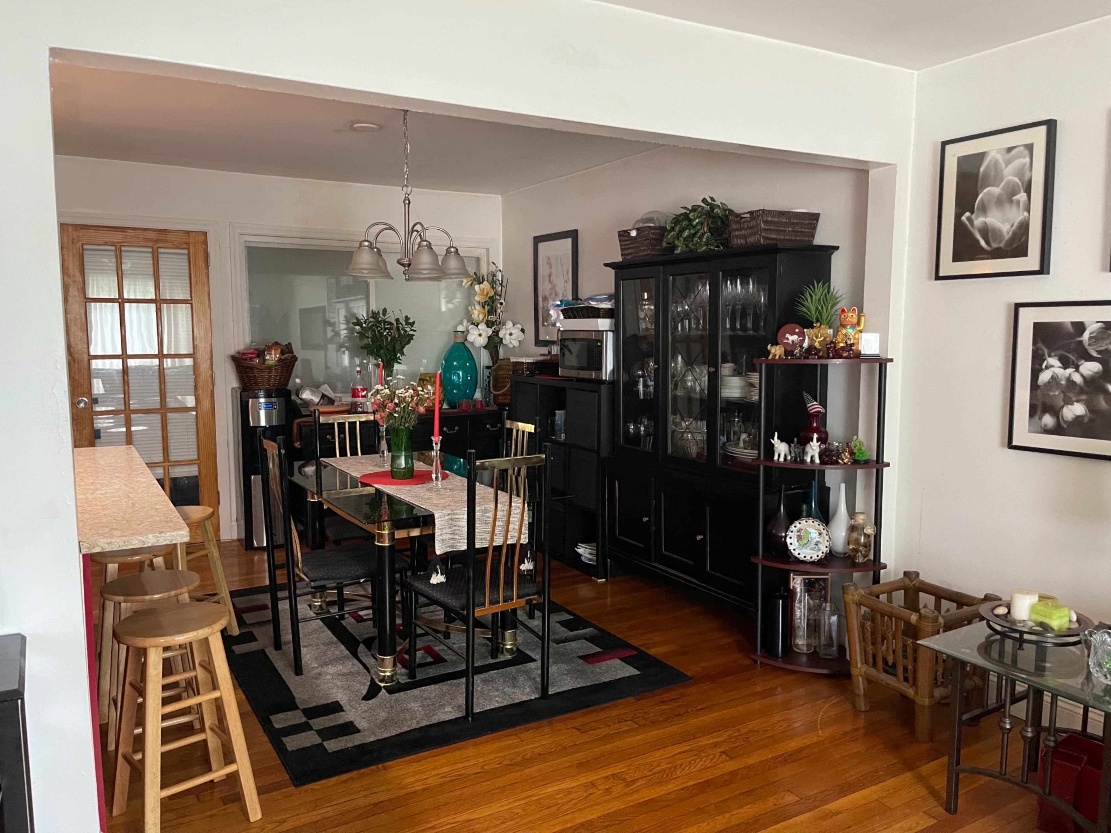 A dining area with a black table surrounded by chairs, a side cabinet filled with glassware, and decorative items on shelves.
