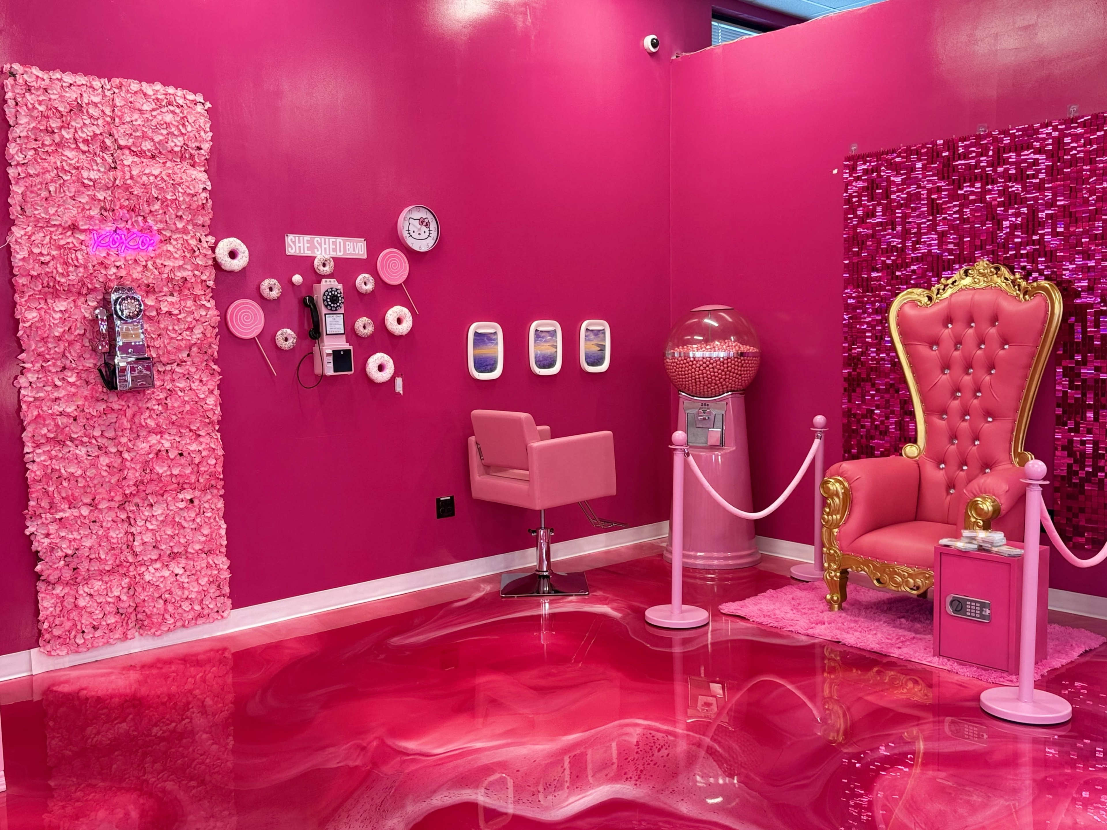 The image shows a vibrant pink room decorated with floral wall art, a glamorous throne chair, and a vintage-style gumball machine.