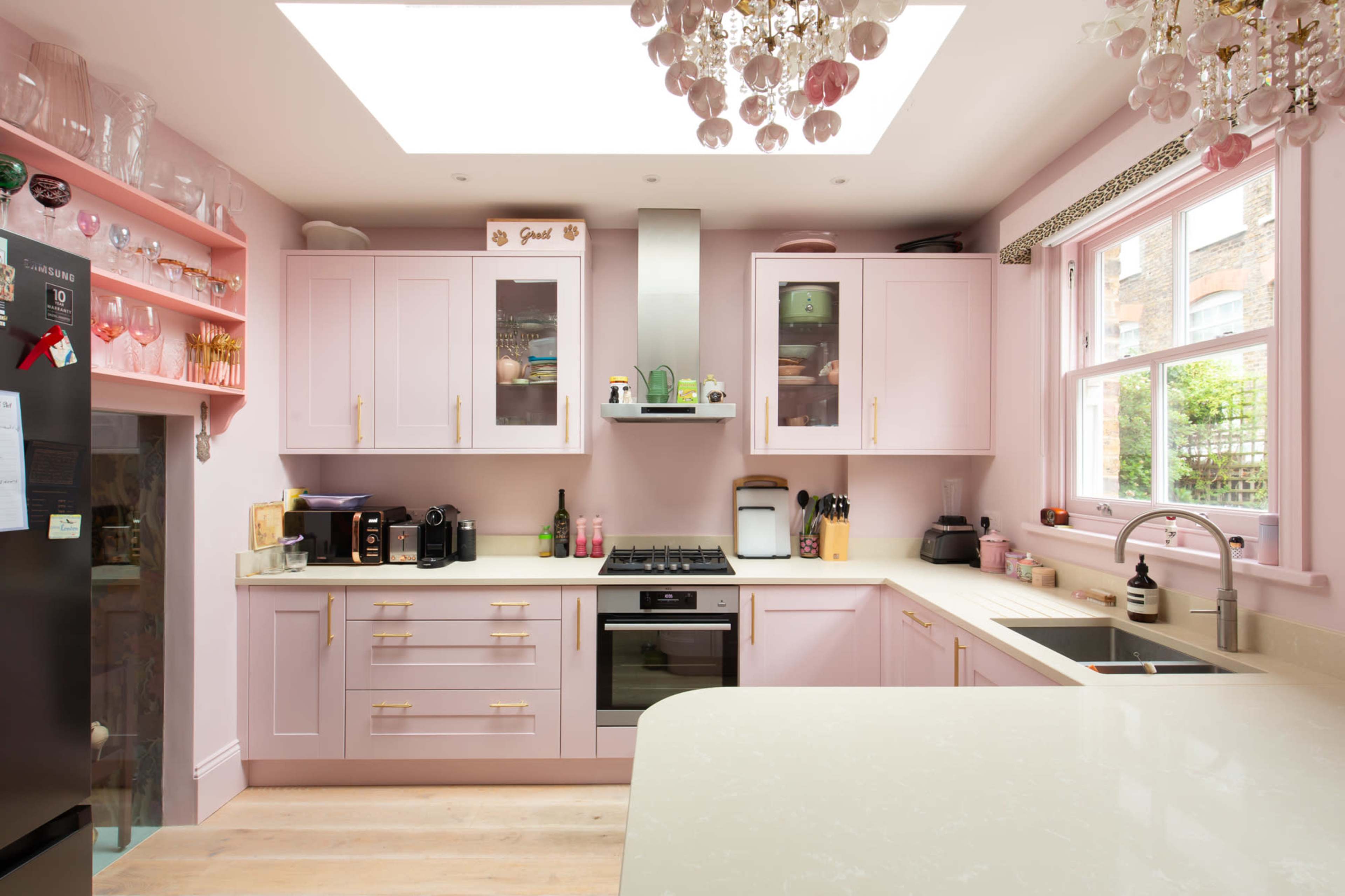 A modern kitchen features pale pink cabinets, a central island with a white countertop, and a chandelier made of glass orbs.
