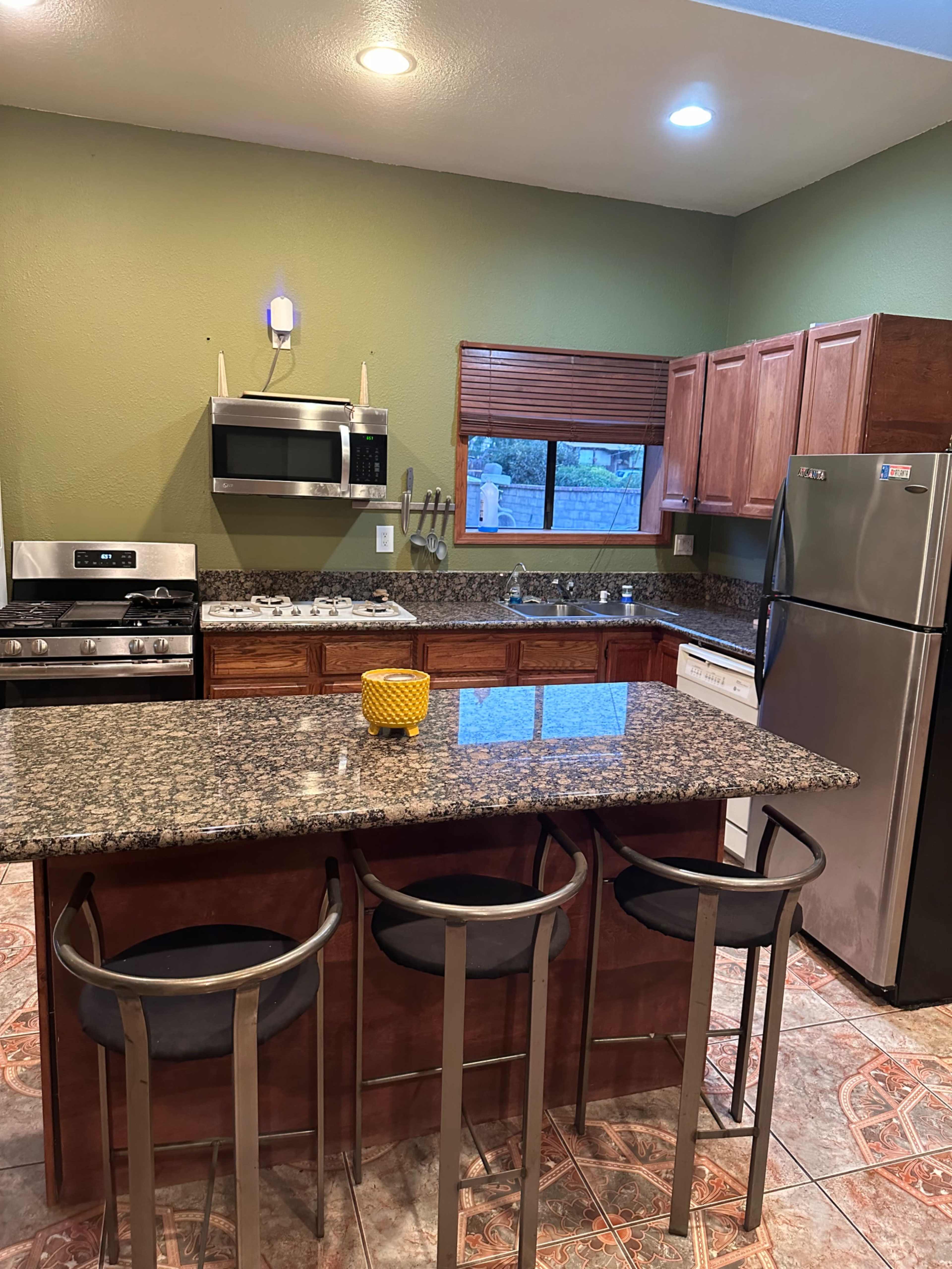 The kitchen features wooden cabinets, a granite countertop island with three stools, and modern appliances including a microwave, stove, and refrigerator.