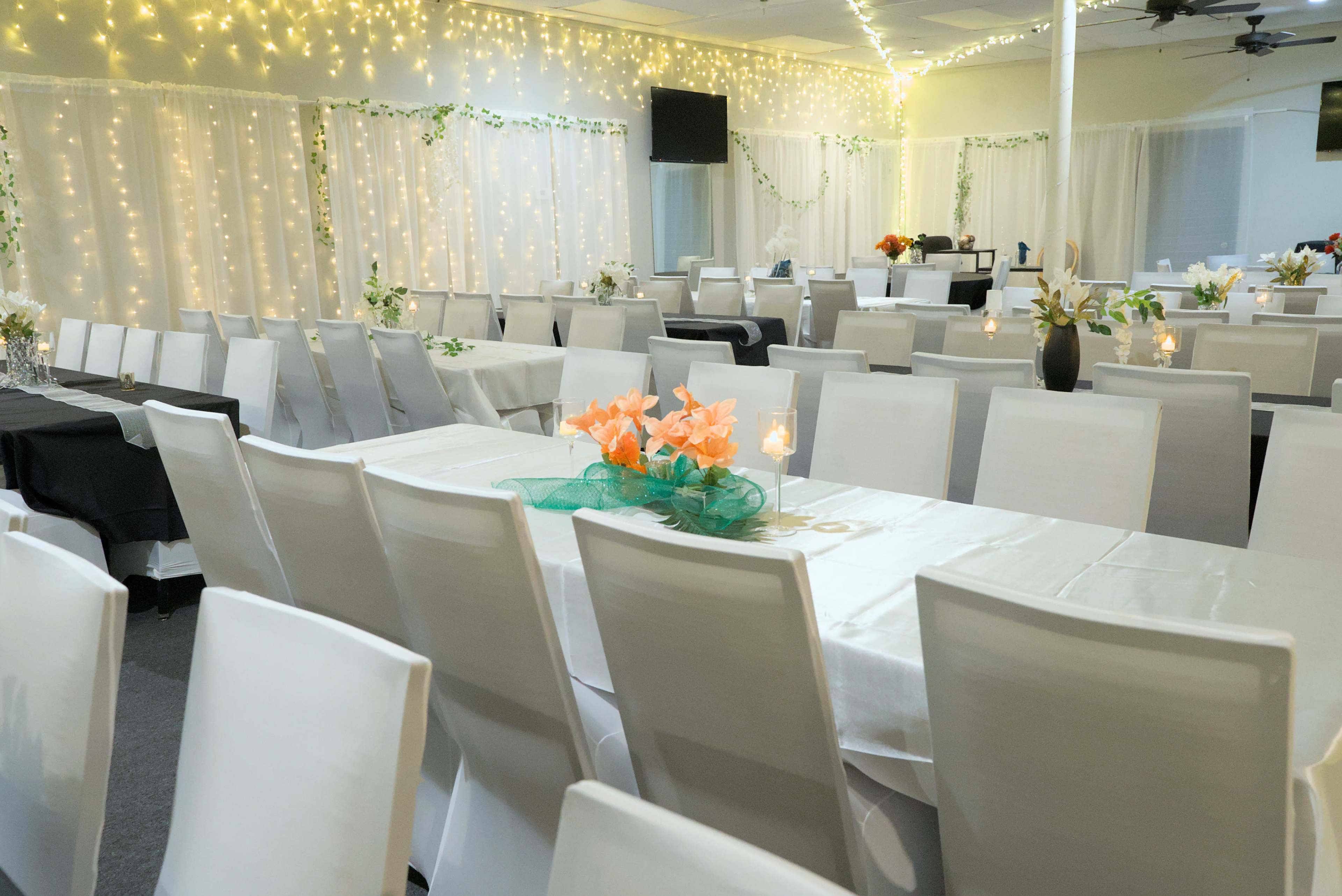 A banquet hall set with white tables and chairs, decorated with flowers and soft lighting.