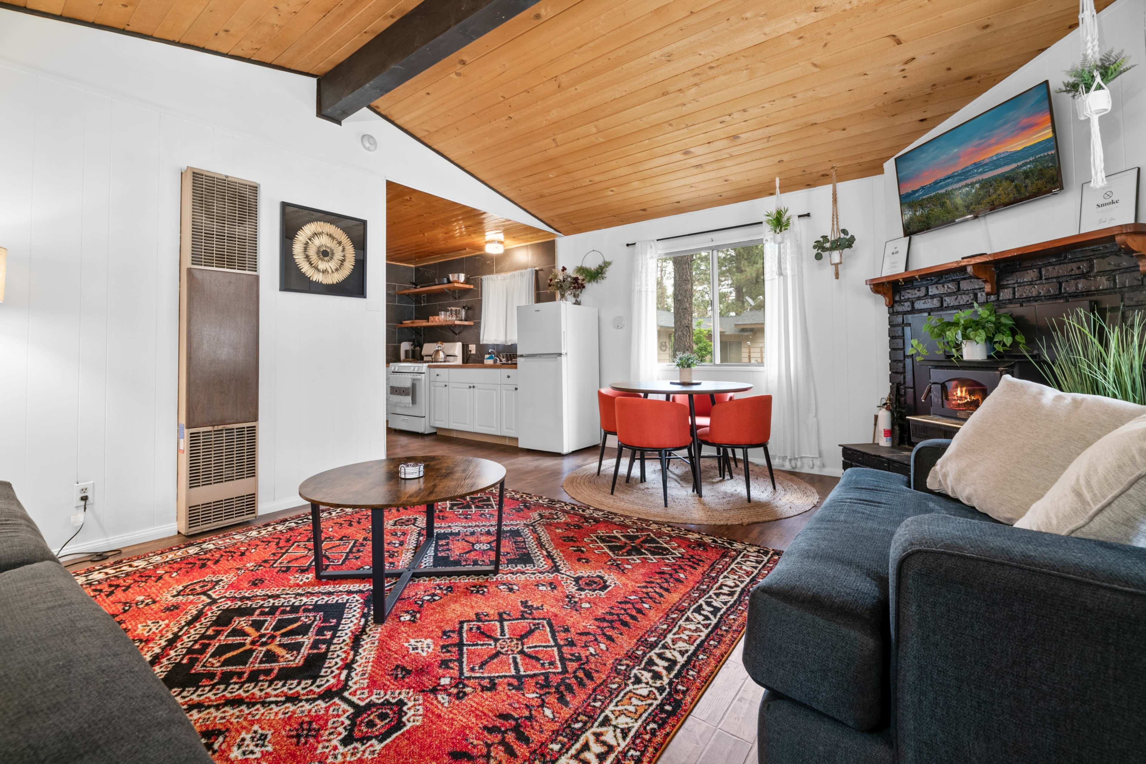 A modern living room with a wooden ceiling, a cozy seating area, a dining table for four, and a fireplace.
