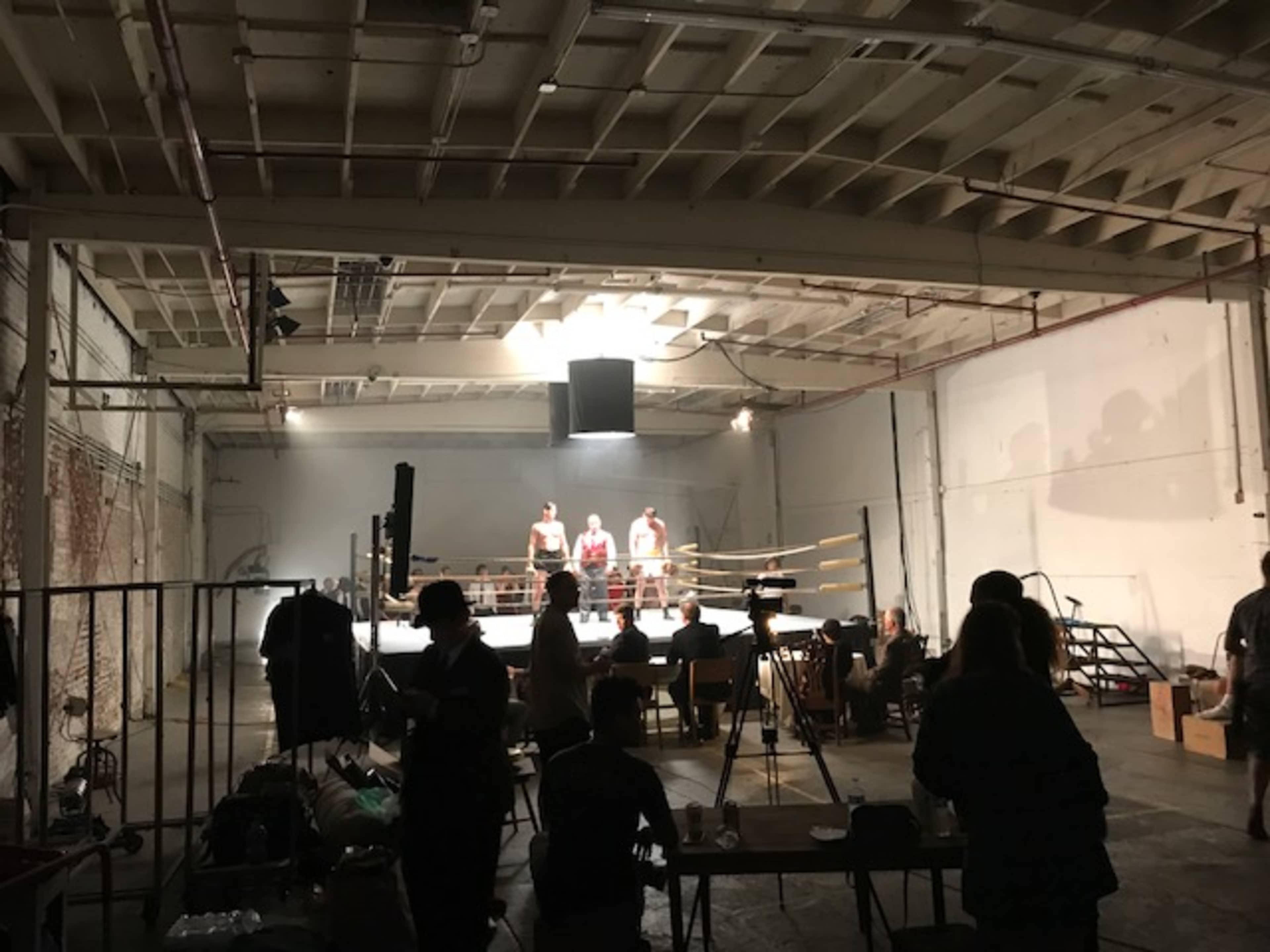 A boxing match taking place in a spacious, well-lit indoor venue, with spectators and crew members present around the ring.