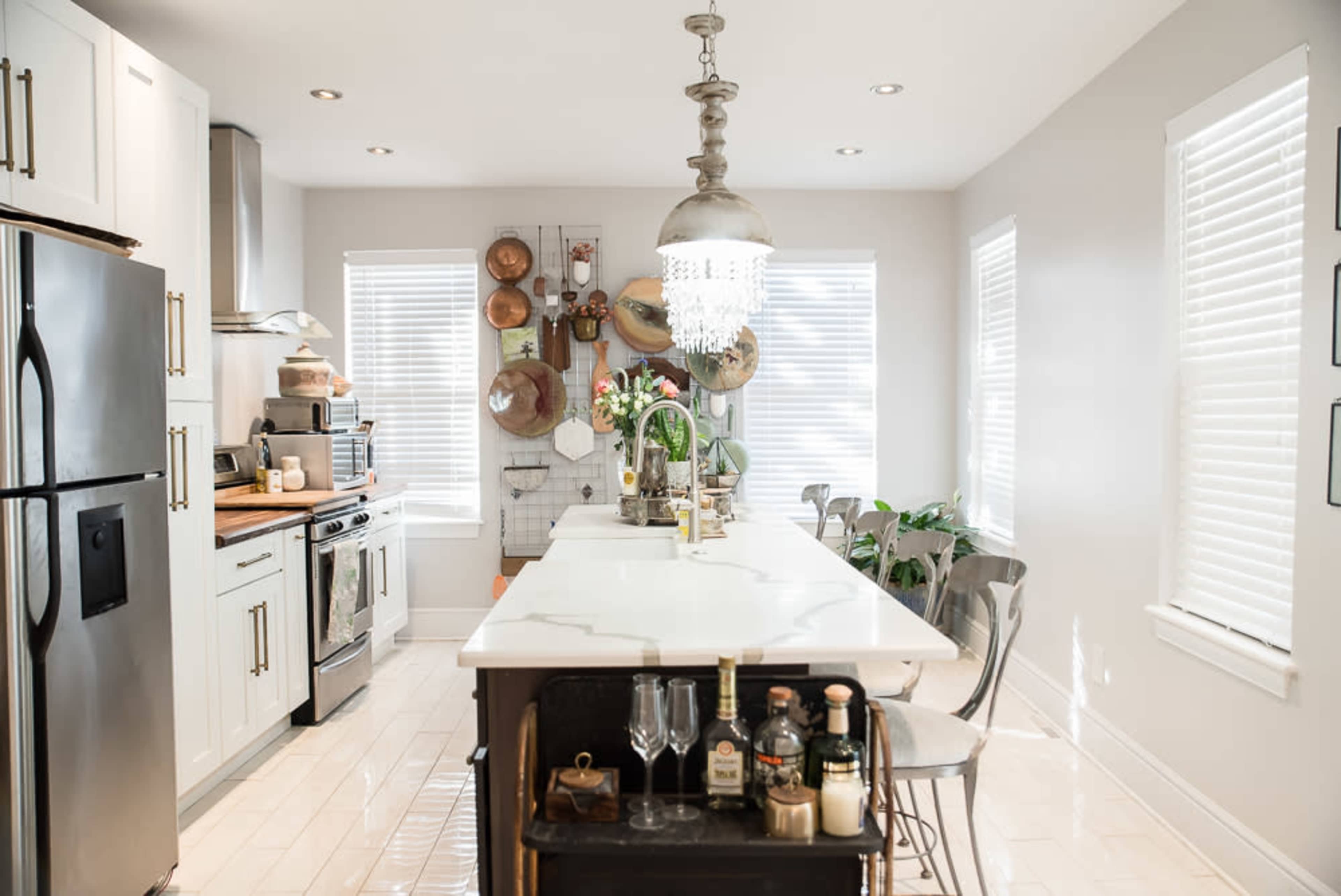 A modern kitchen features a central island with bar stools, stainless steel appliances, and decorative wall-mounted cookware.