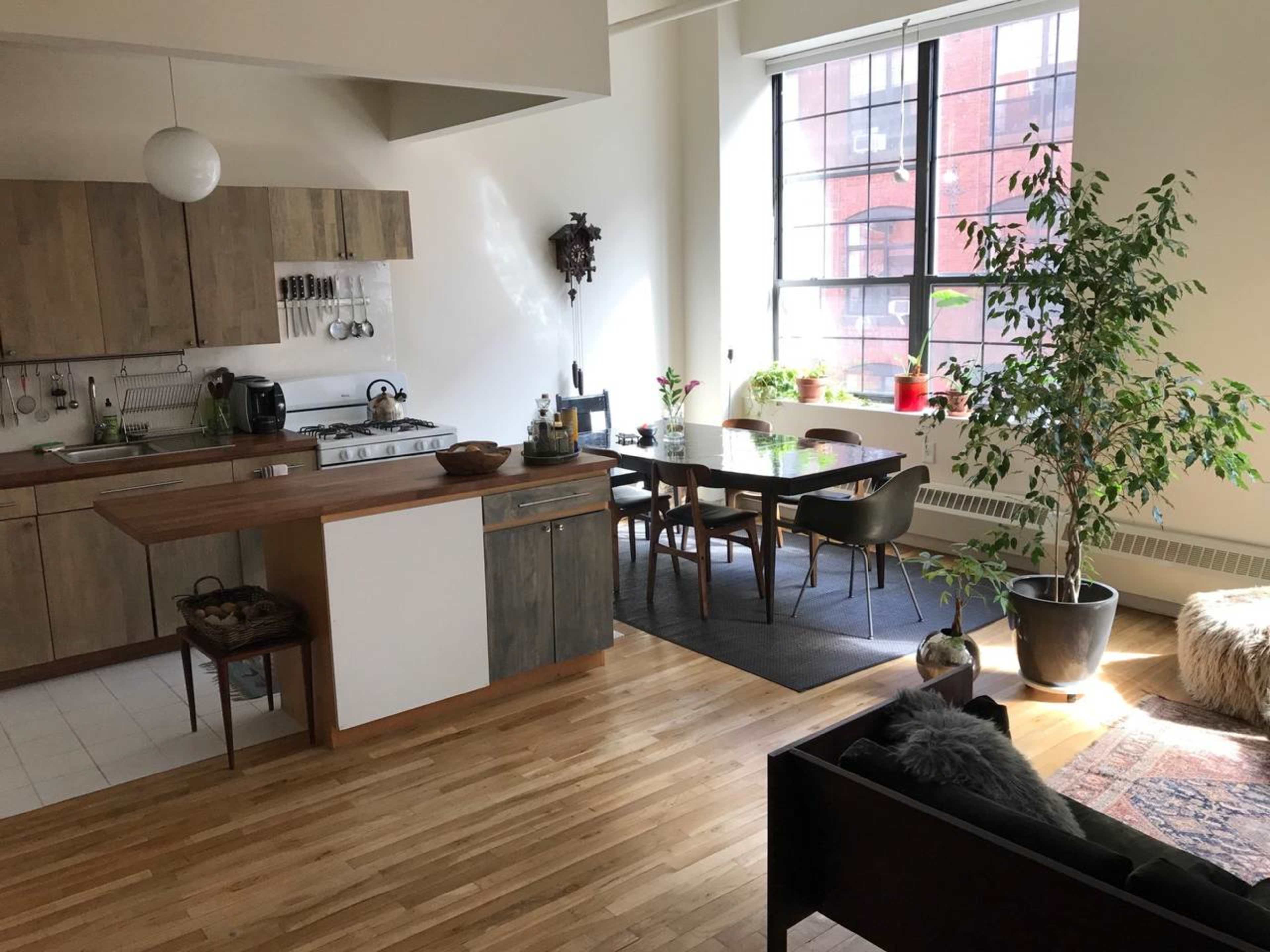 A modern kitchen and dining area feature wooden cabinetry, a dining table with chairs, and a large window letting in natural light.