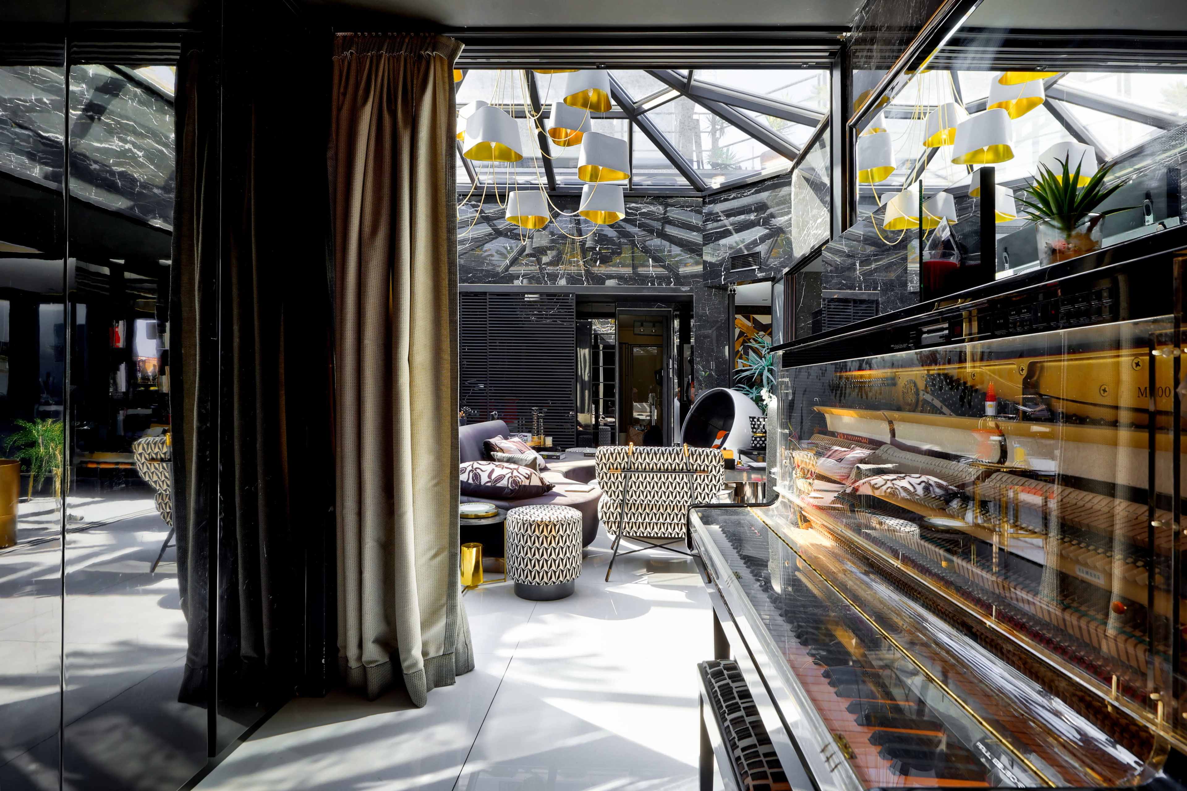 The image shows a modern, elegantly designed lounge area with a grand piano, large windows, and contemporary furnishings.