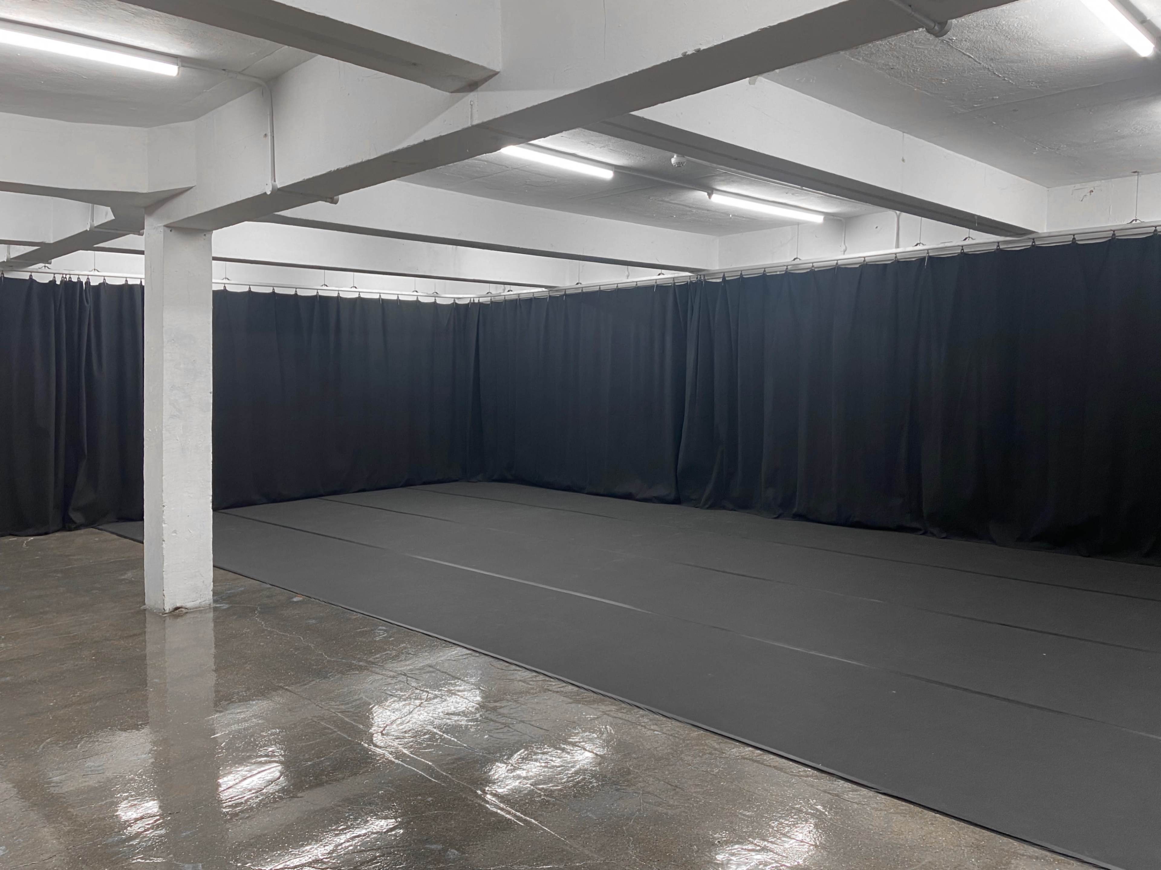 A large, empty rehearsal space with black curtains lining the walls and a dark, reflective floor.