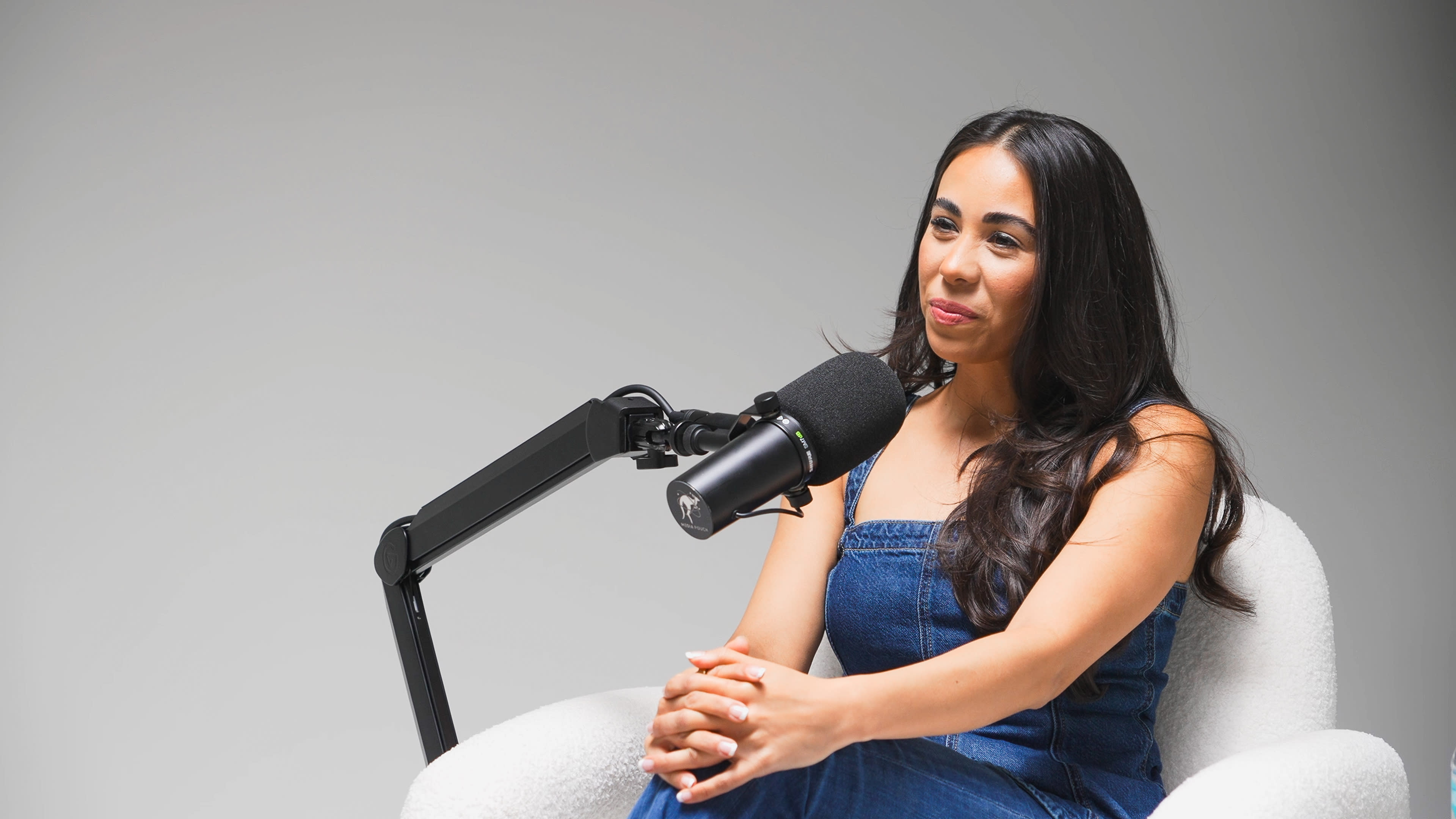 A woman sits in a chair, speaking into a microphone that is mounted on an adjustable arm.