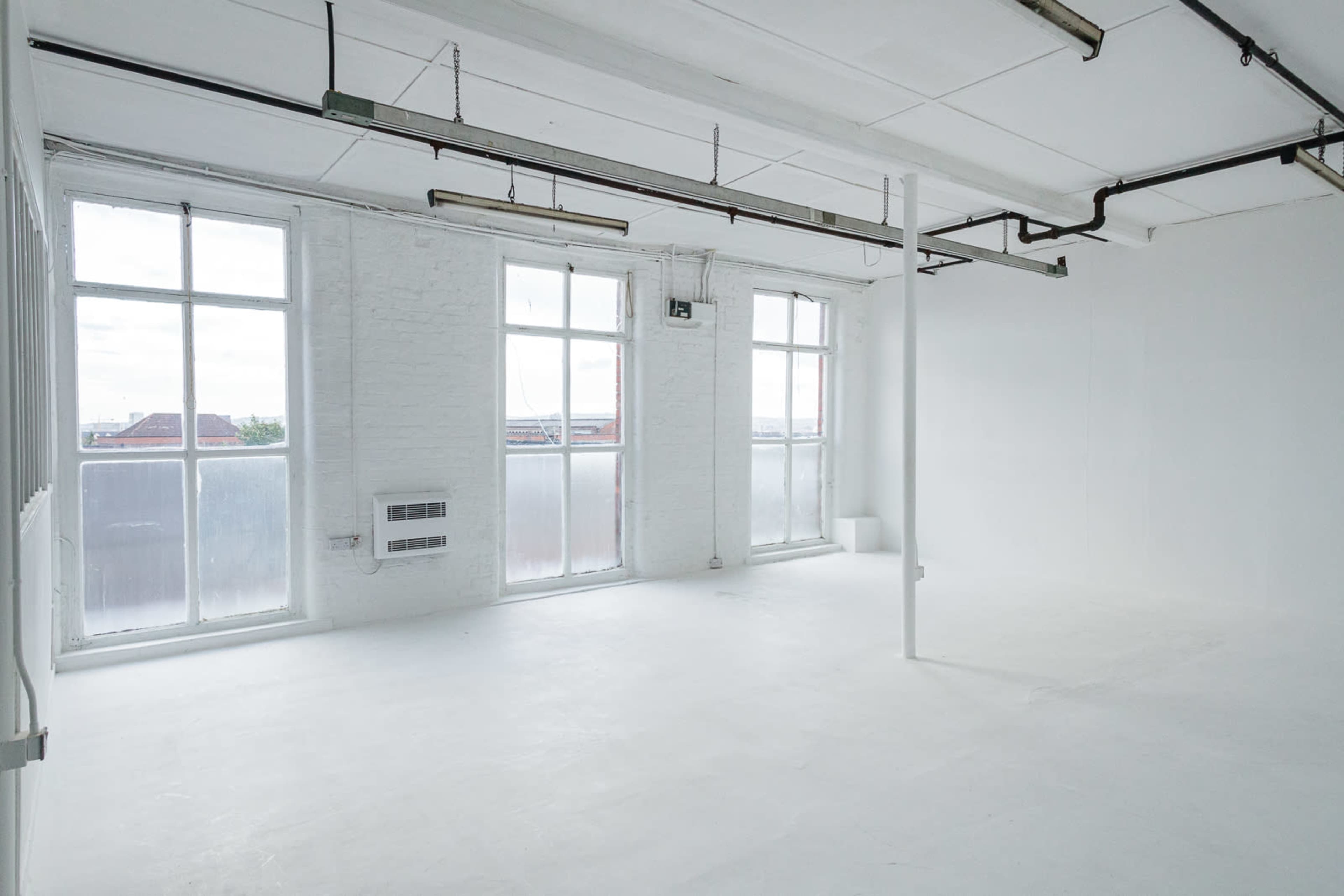 A bright, empty room with large windows, white walls, and a polished concrete floor.