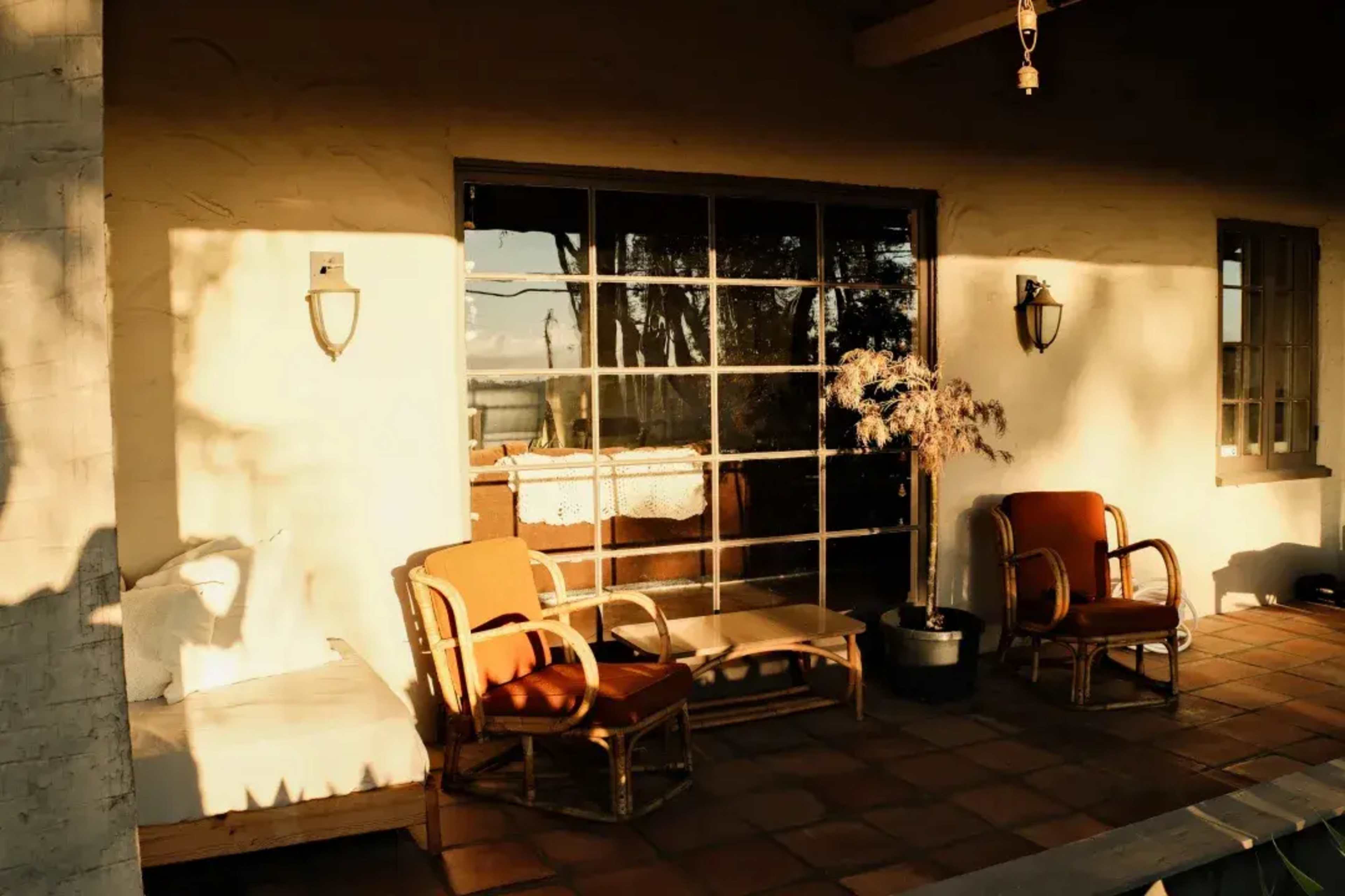 The image shows a cozy porch with two orange chairs, a small table, and a window displaying a view outside.