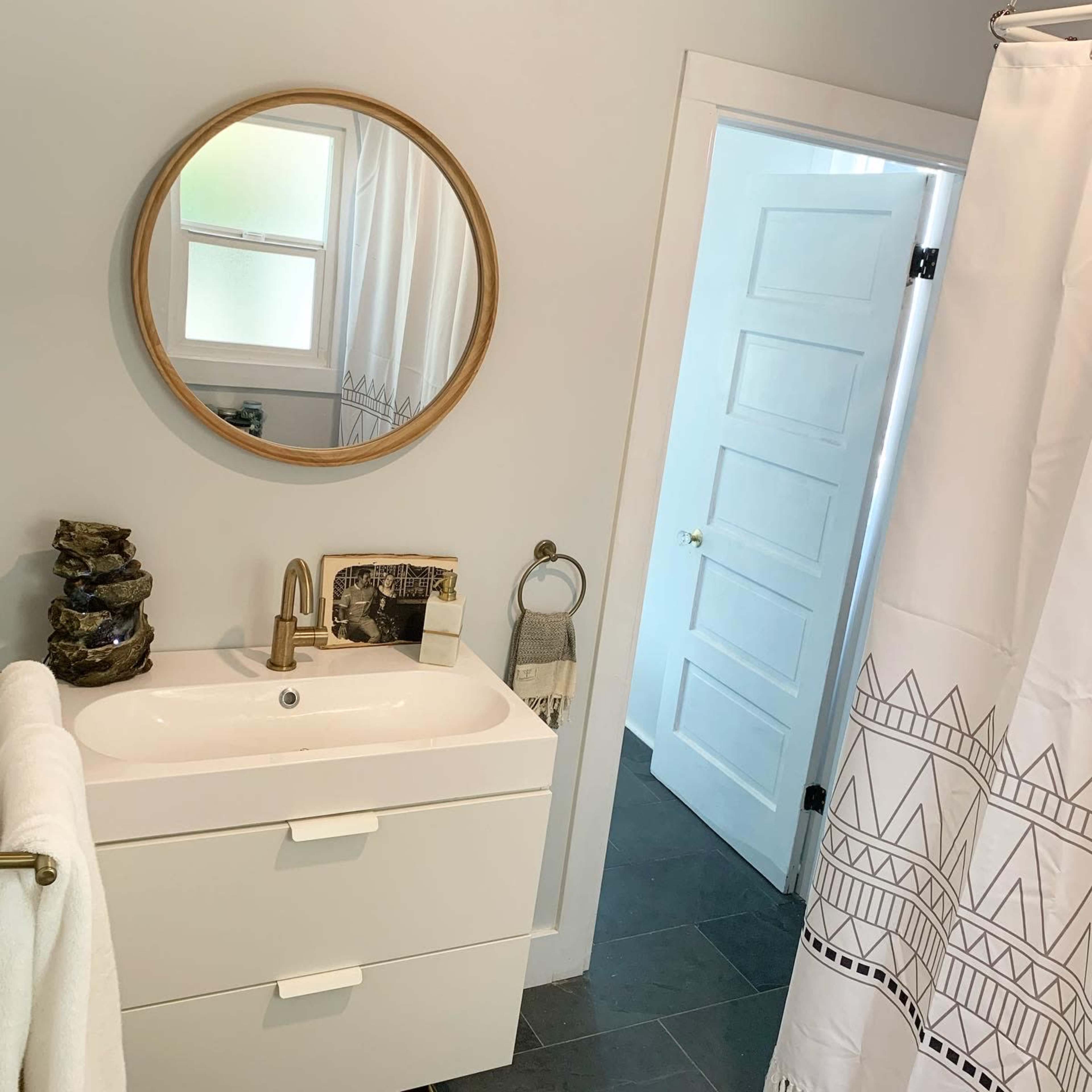 A modern bathroom with a circular mirror above a white vanity and a door leading to another room.