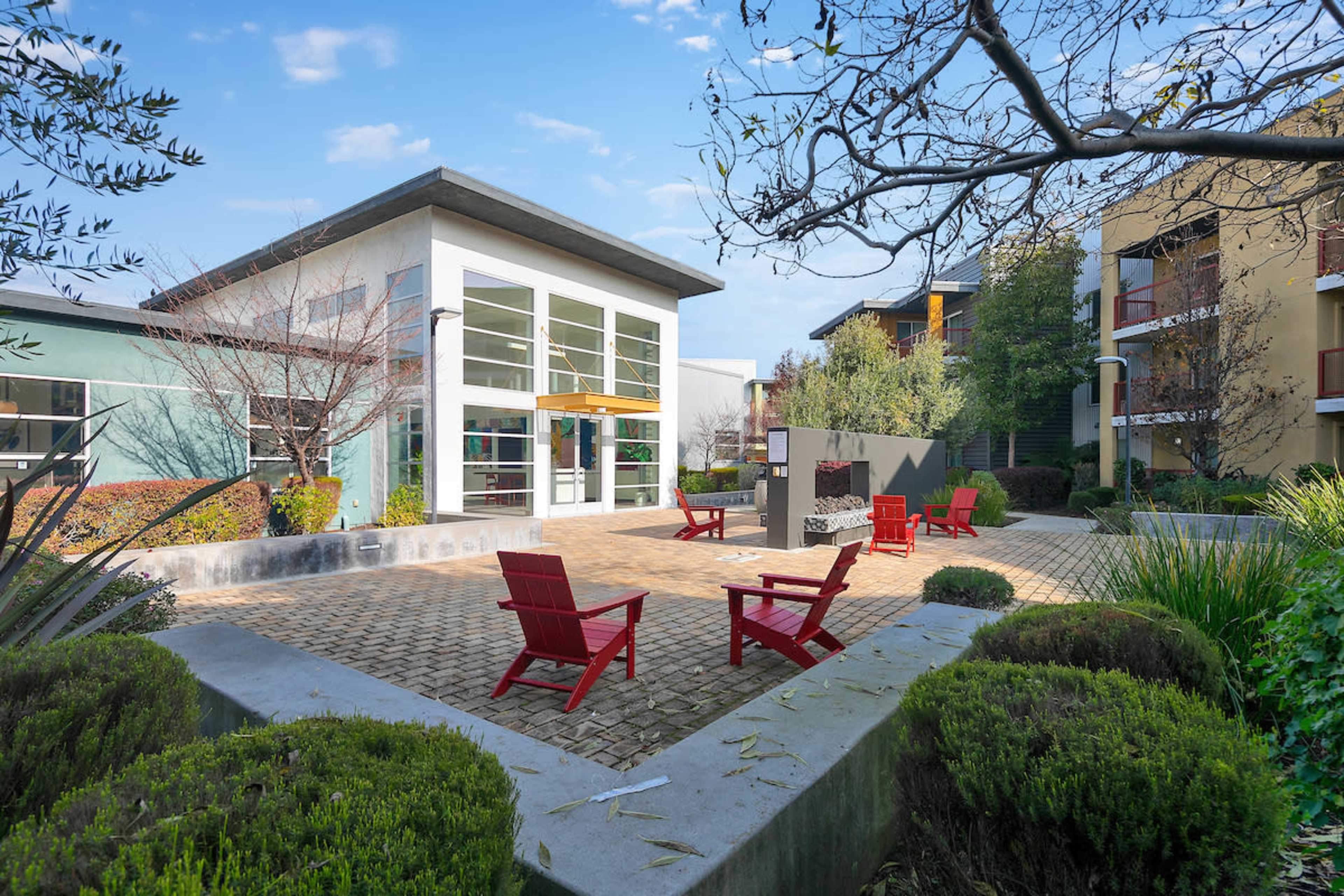A courtyard featuring red chairs, surrounded by greenery and buildings.