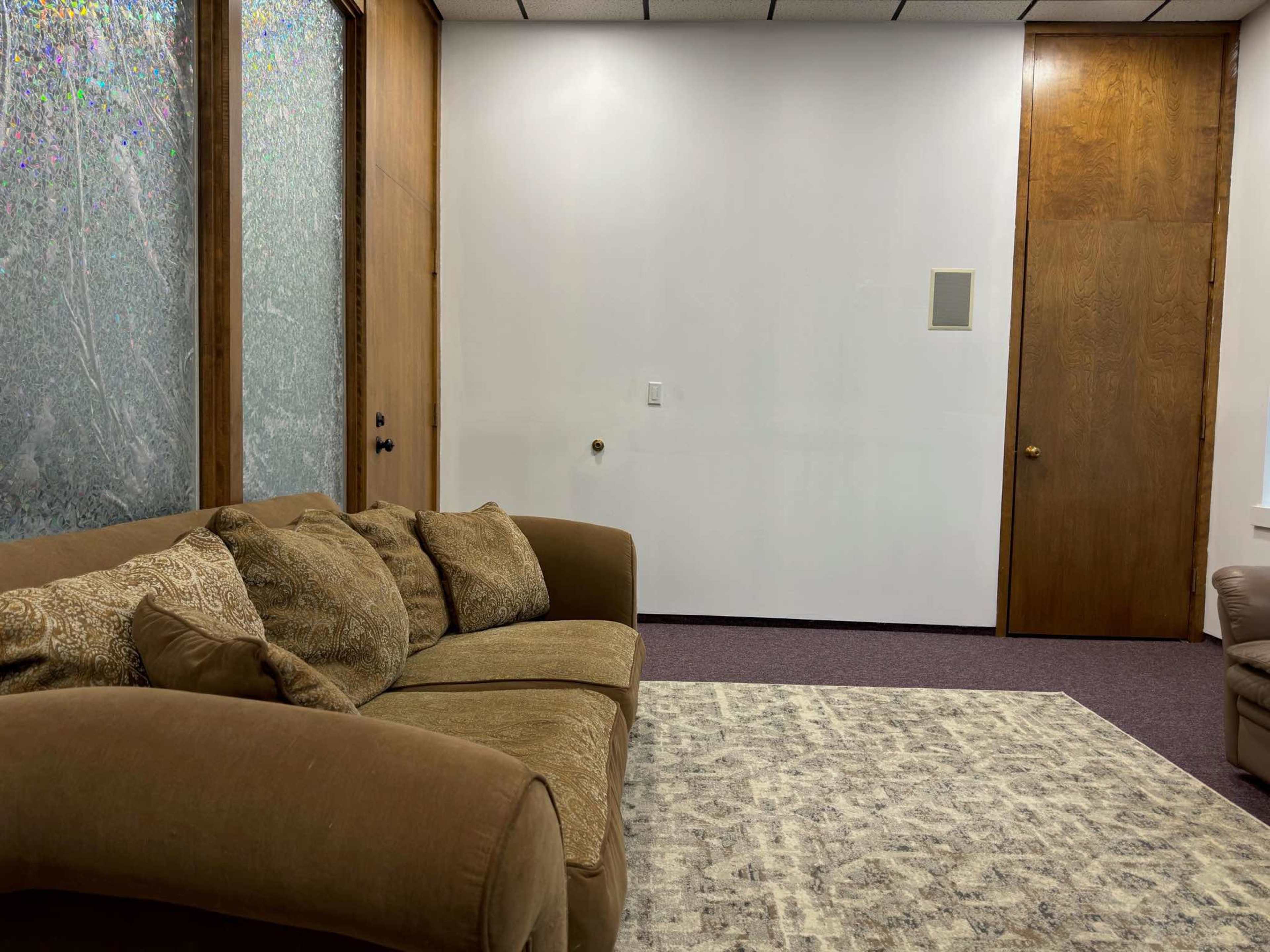 The room features a brown sofa facing a wall with a door and a textured glass panel.