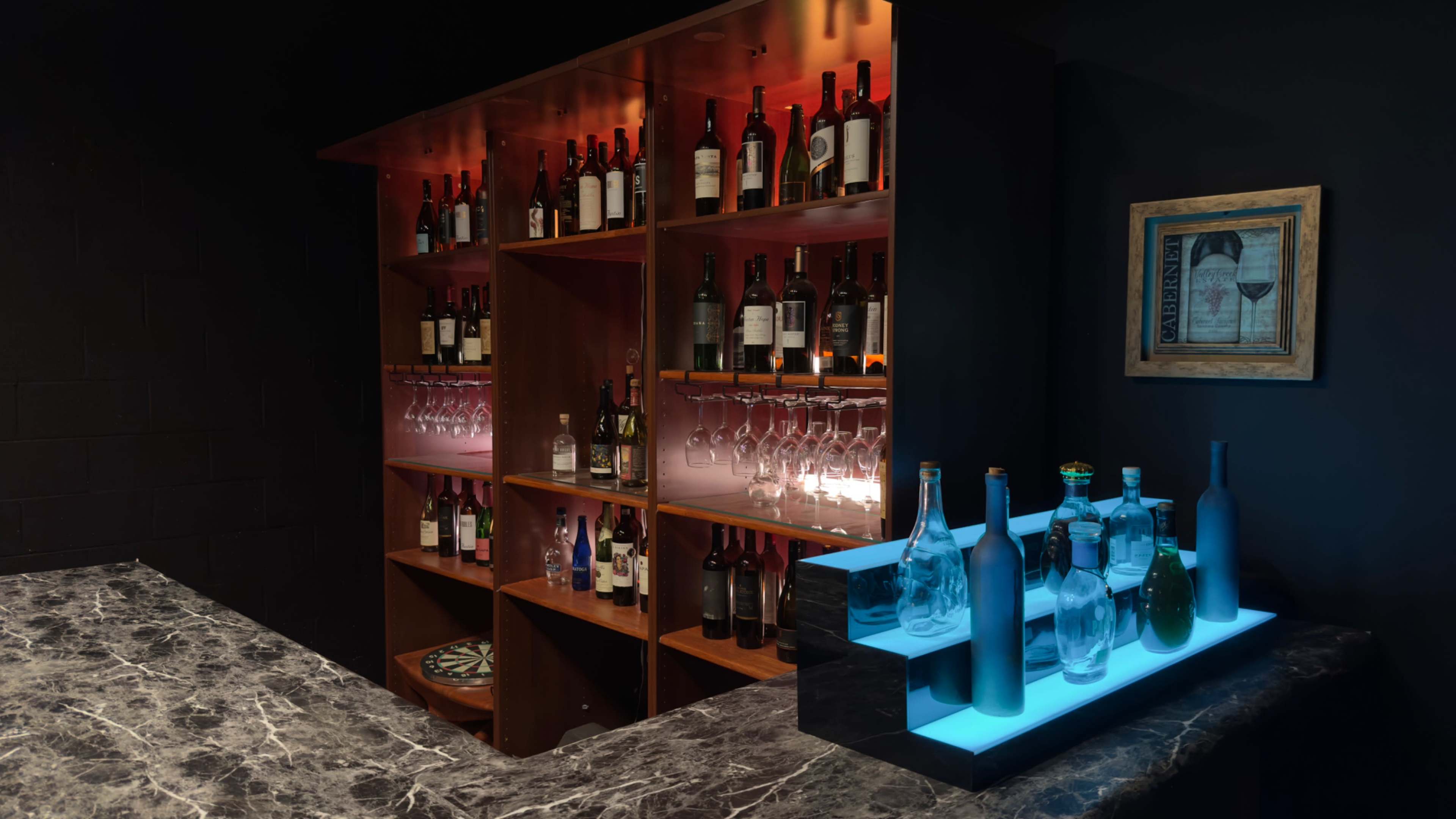 A well-organized bar area with shelves stocked with various bottles of wine and spirits, alongside a lighted display featuring several glass bottles.
