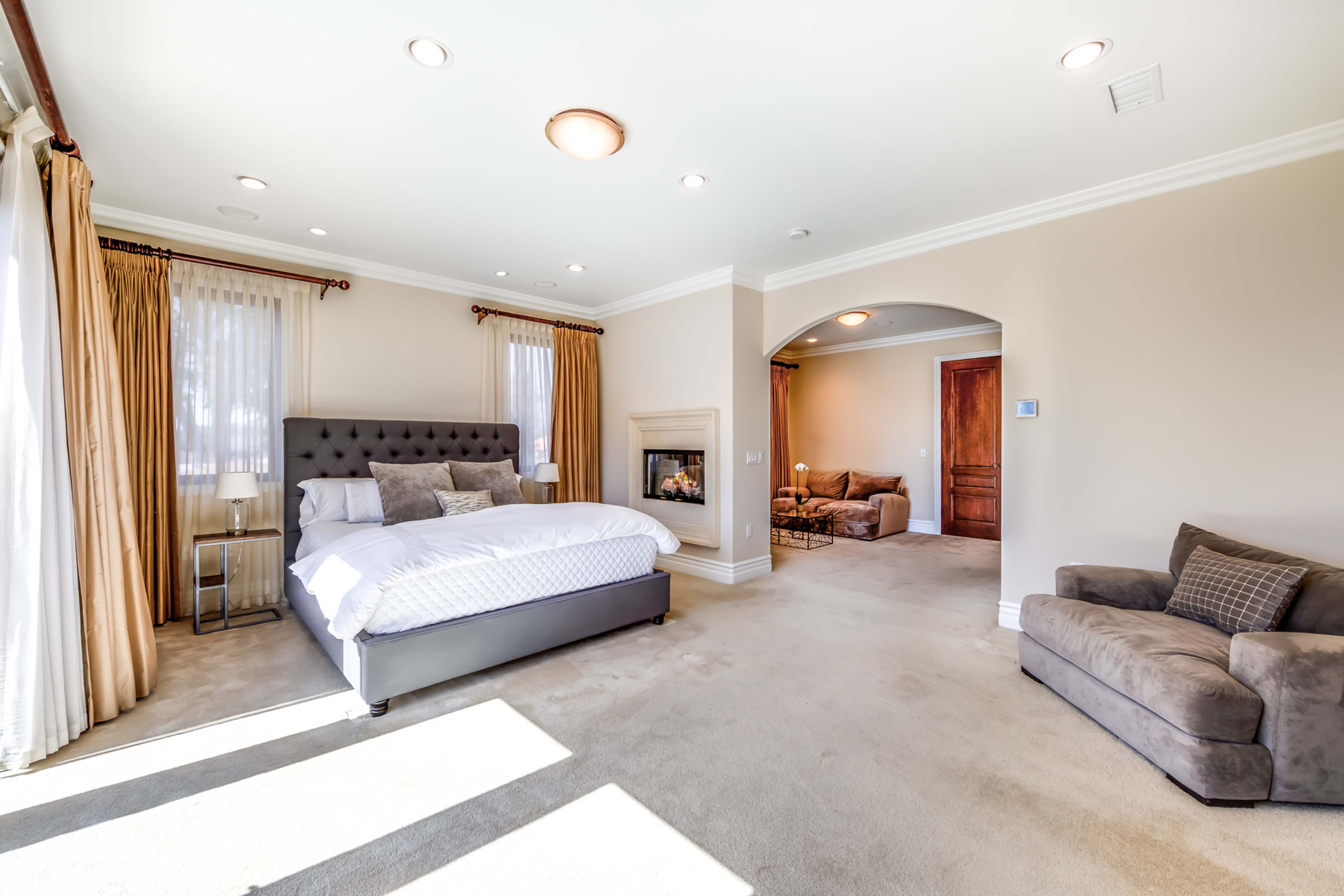 The image shows a spacious bedroom featuring a king-sized bed, a fireplace, and a seating area with a sofa.