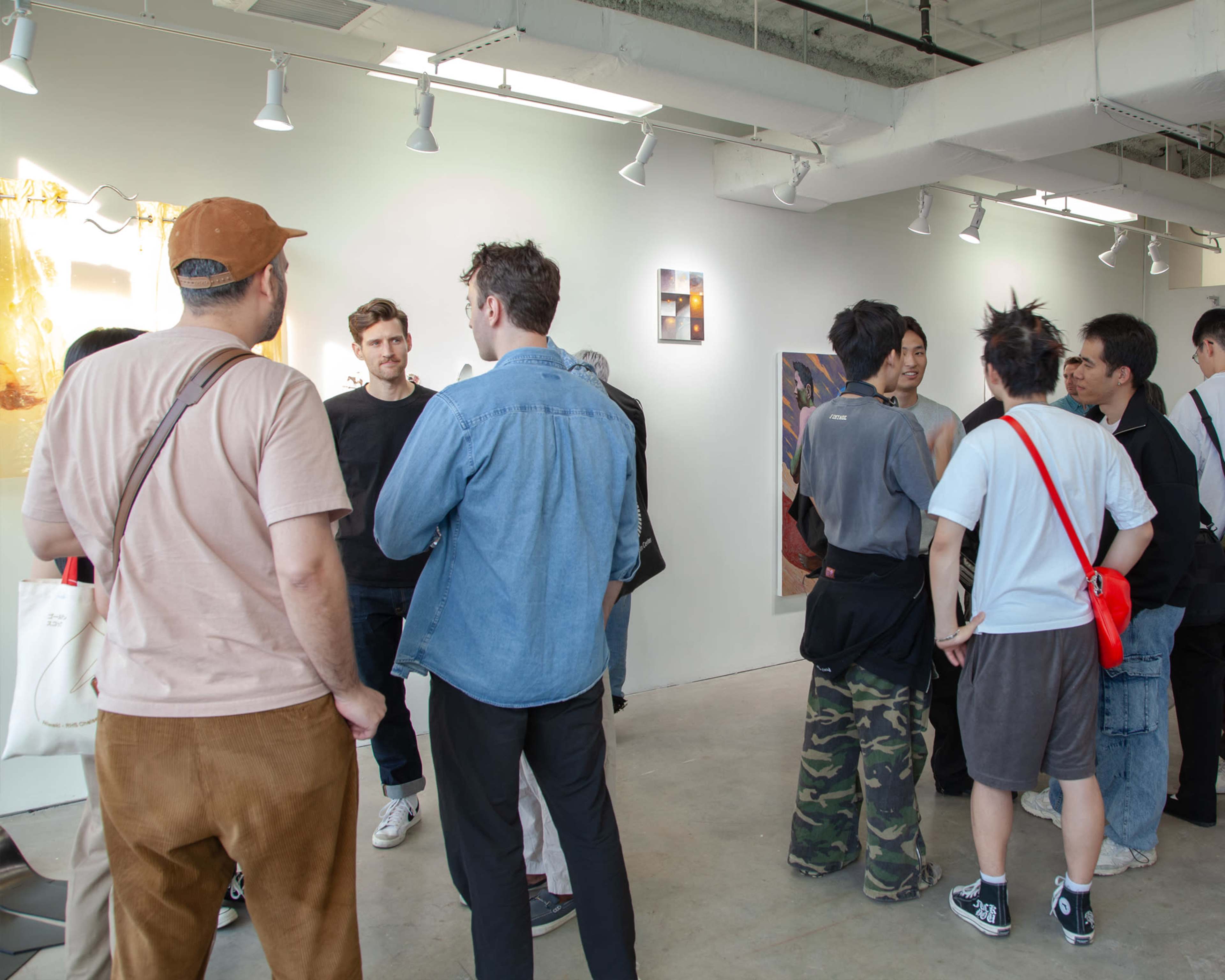 A group of people is engaged in conversation in an art gallery, surrounded by various artworks displayed on the walls.
