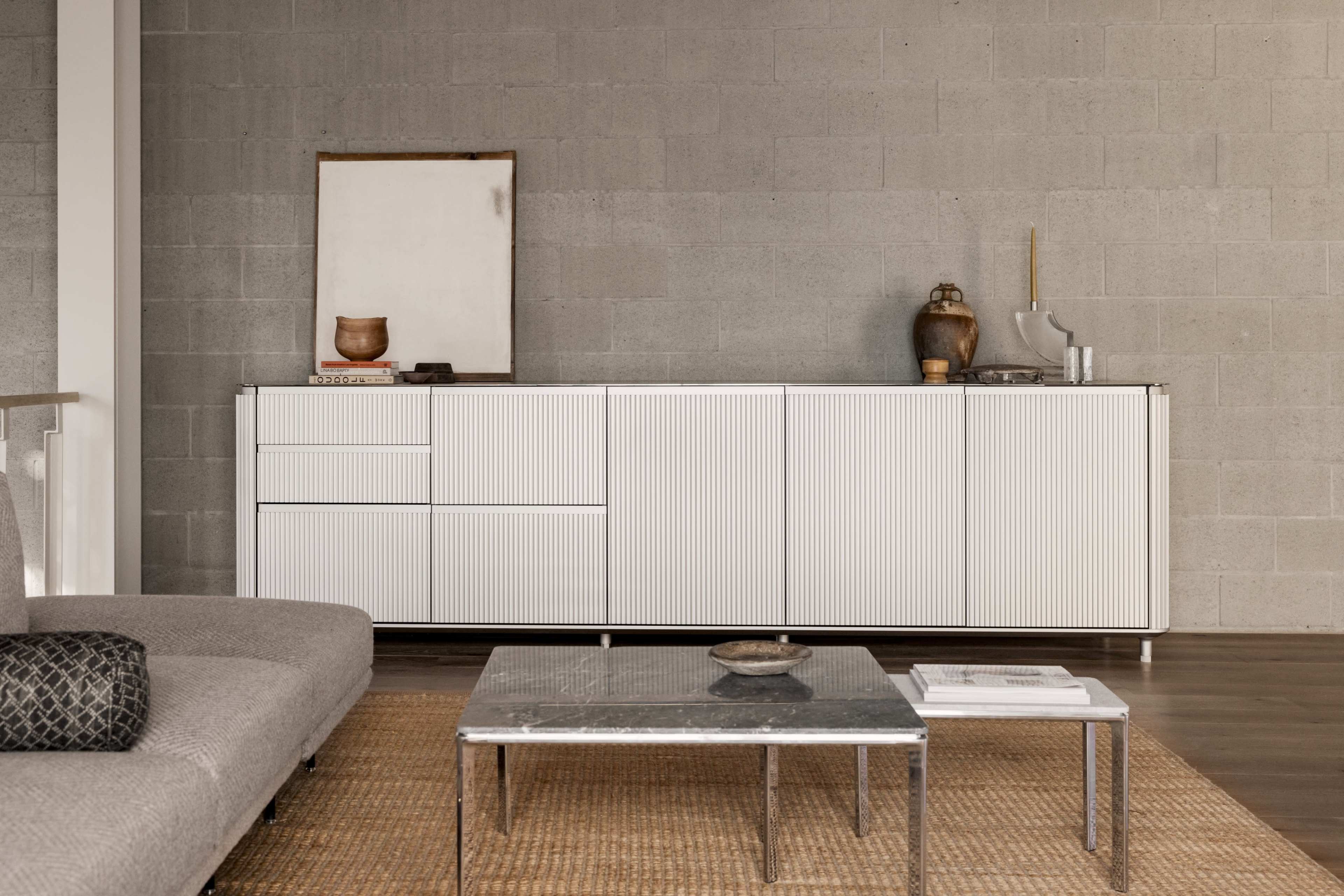 A modern living room features a white sideboard against a gray concrete wall, complemented by a low coffee table and a textured rug.